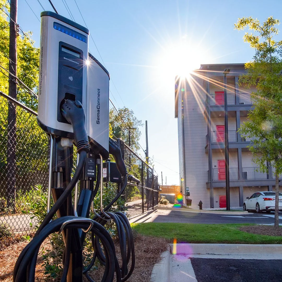Electric vehicle charging station with charging cables plugged in, located outdoors near a residential building Axel Row Birmingham AL - project by B Group Architecture, Inc.