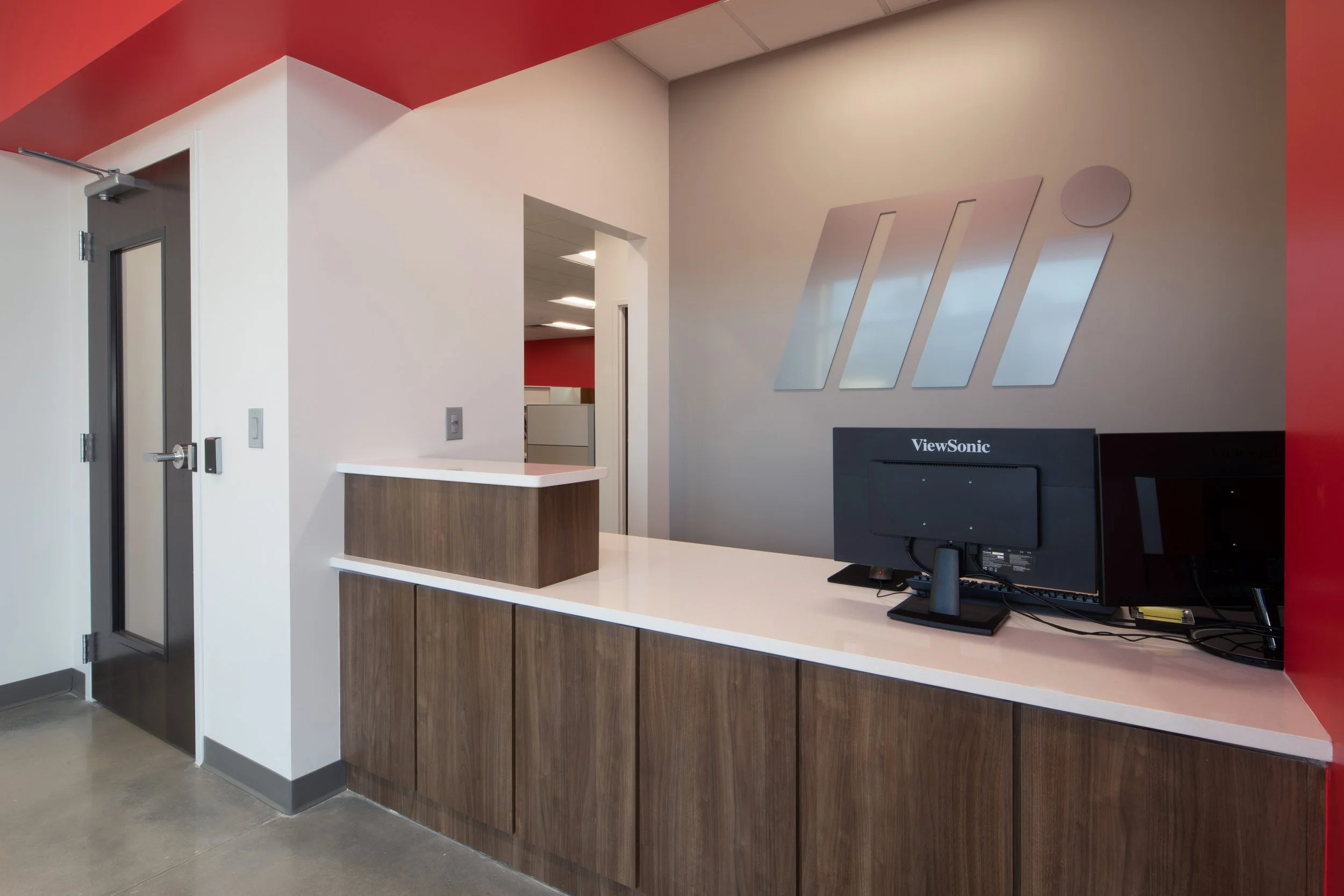 An Interior view of a reception area with a counter with Motion Industries  Mi logo on the wall. project by B Group Architecture, Inc.