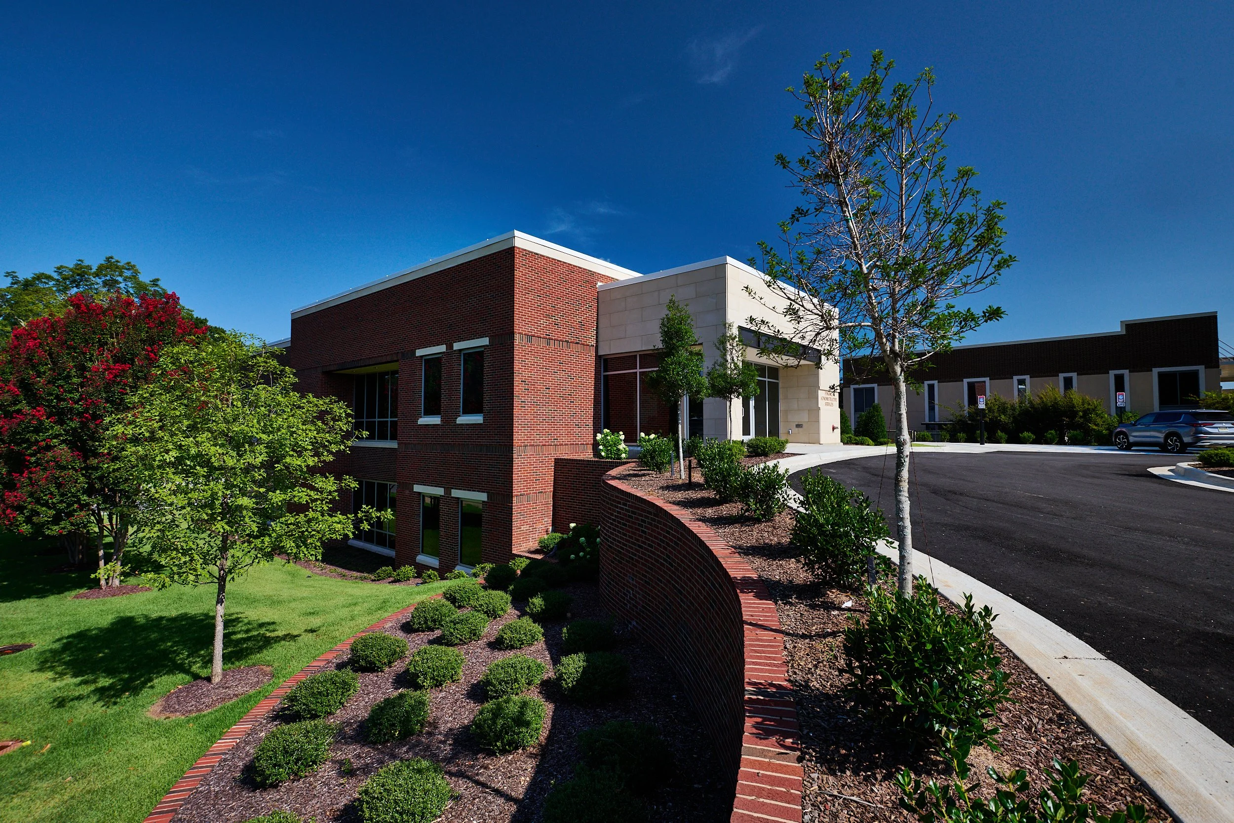 Renovation of the University of Alabama Administration Building. This brick building with large windows and accentuated by cast stone, surrounded by a retaining wall and well-maintained landscaping-project by B Group Architecture, Inc.
