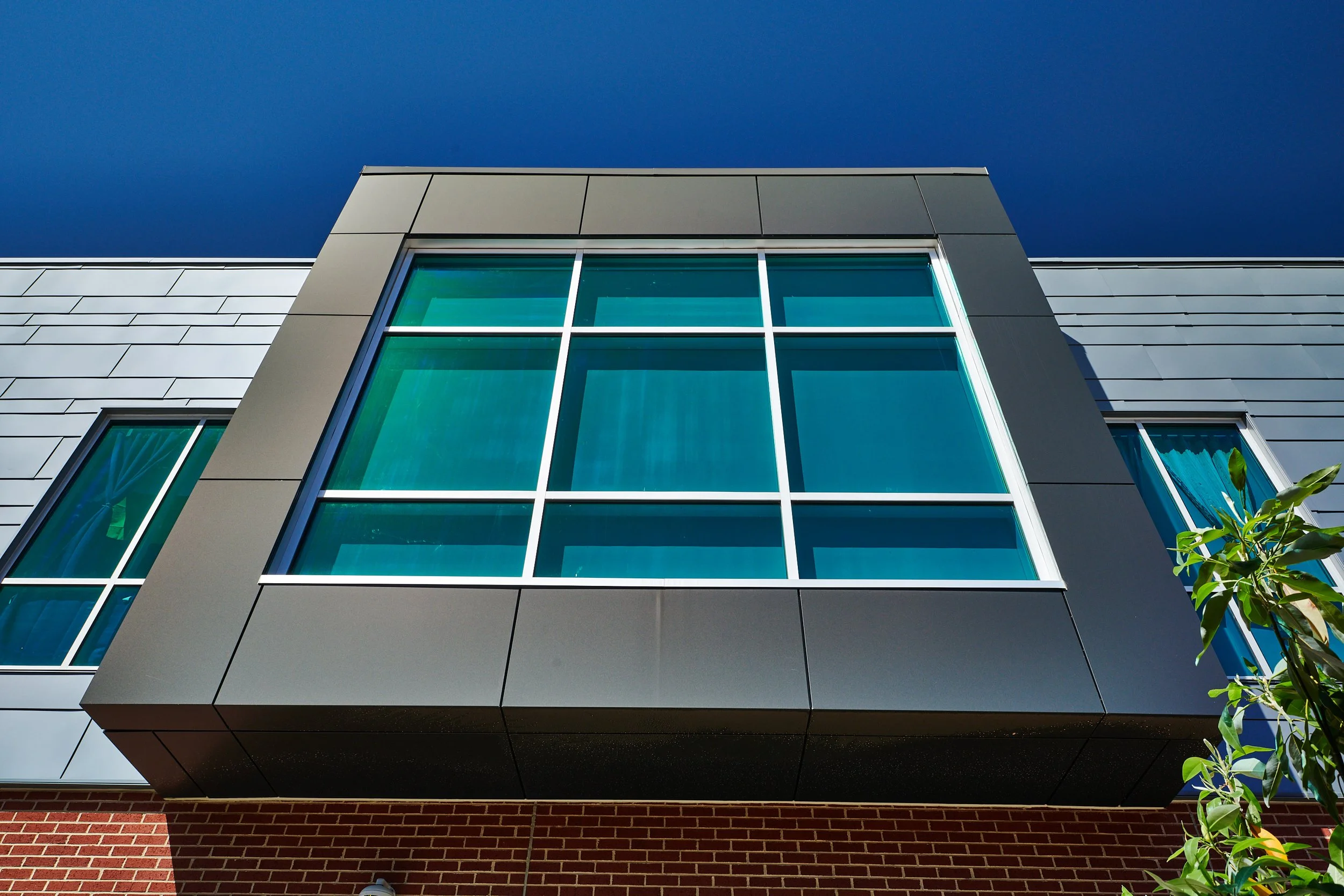 Modern building facade with Kawneer curtainwall and storefront glass windows, varying sized metal paneling with a brick base - project by B Group Architecture, Inc.
