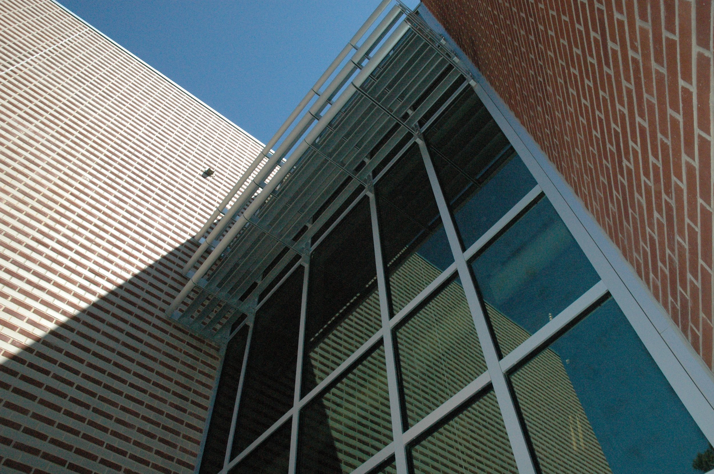 Low-angle view of a modern high school building with patterned brick walls, glass curtainwall windows, and metal sun shades.- project by B Group Architecture, Inc.