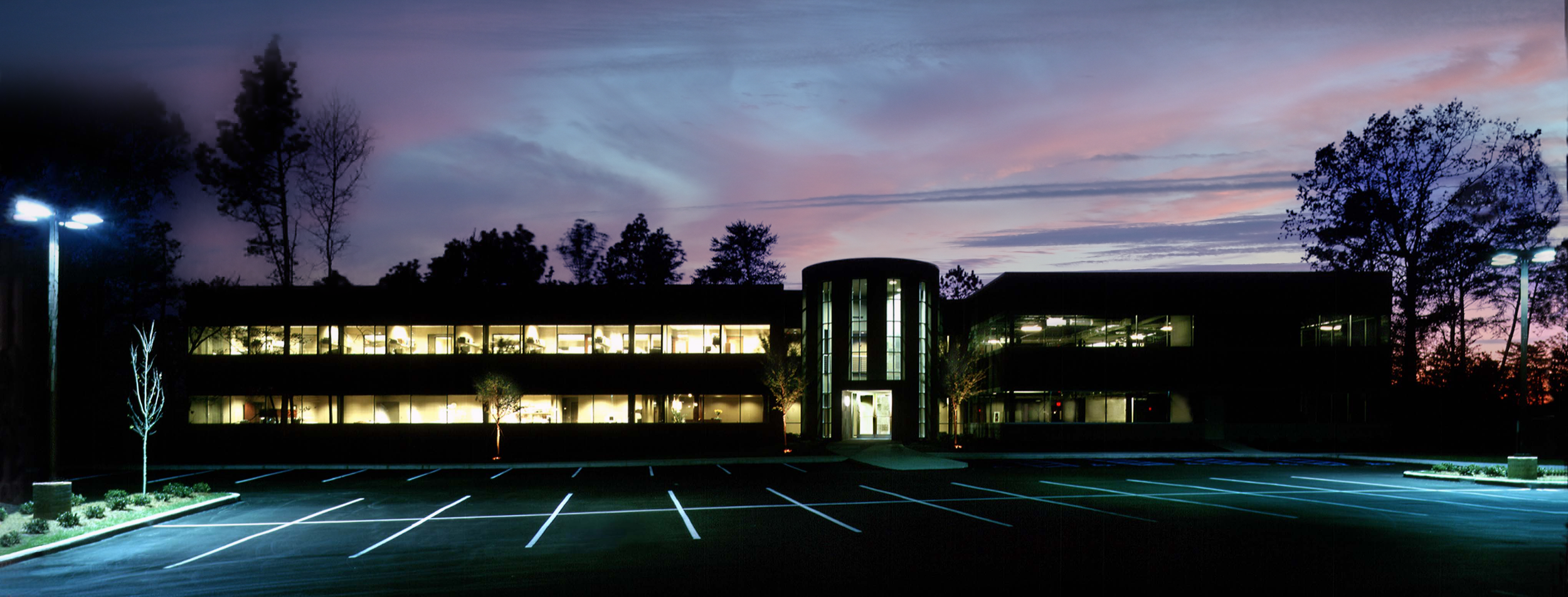 Exterior night view of River Ridge Centre showcasing glass and brick banding highlighted by a glass circulation tower. project  by B Group Architecture, Inc.