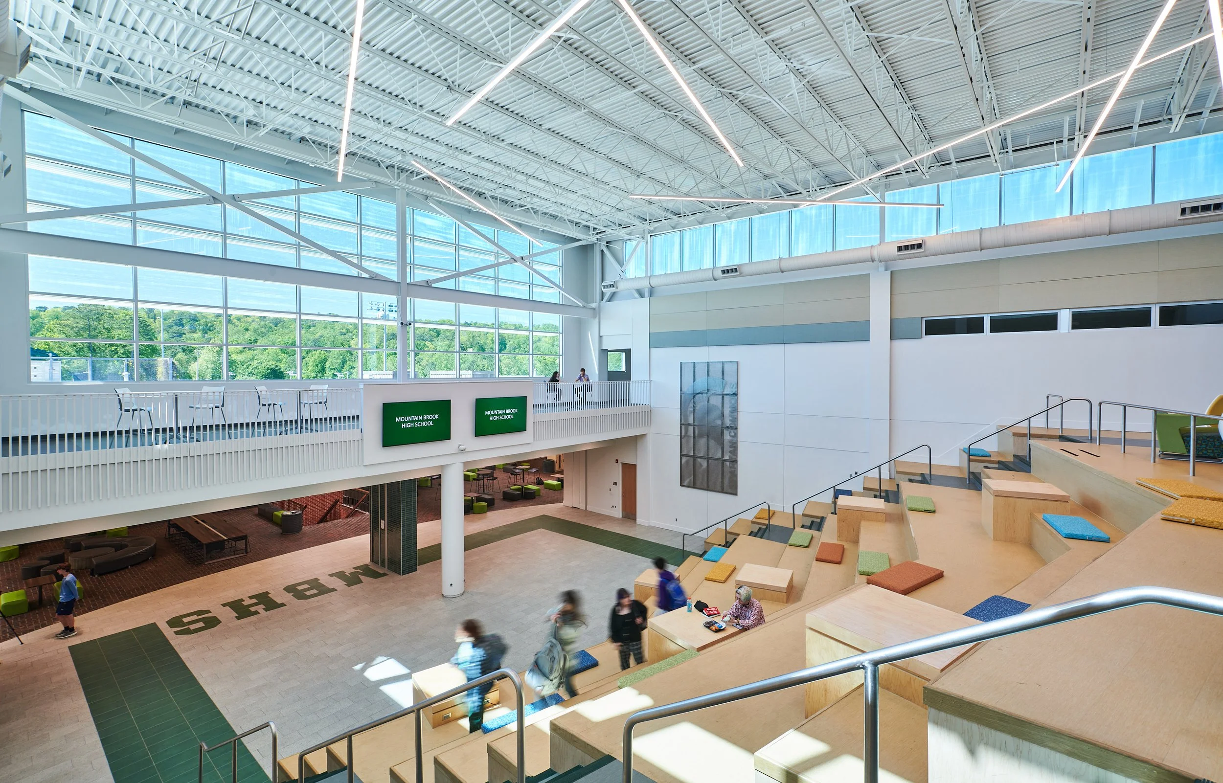 Interior view of a modern High School with the tiered cushioned seating and stairs  showcasing large clerestory insulated windows and exposed structure- project by B Group Architecture, Inc.