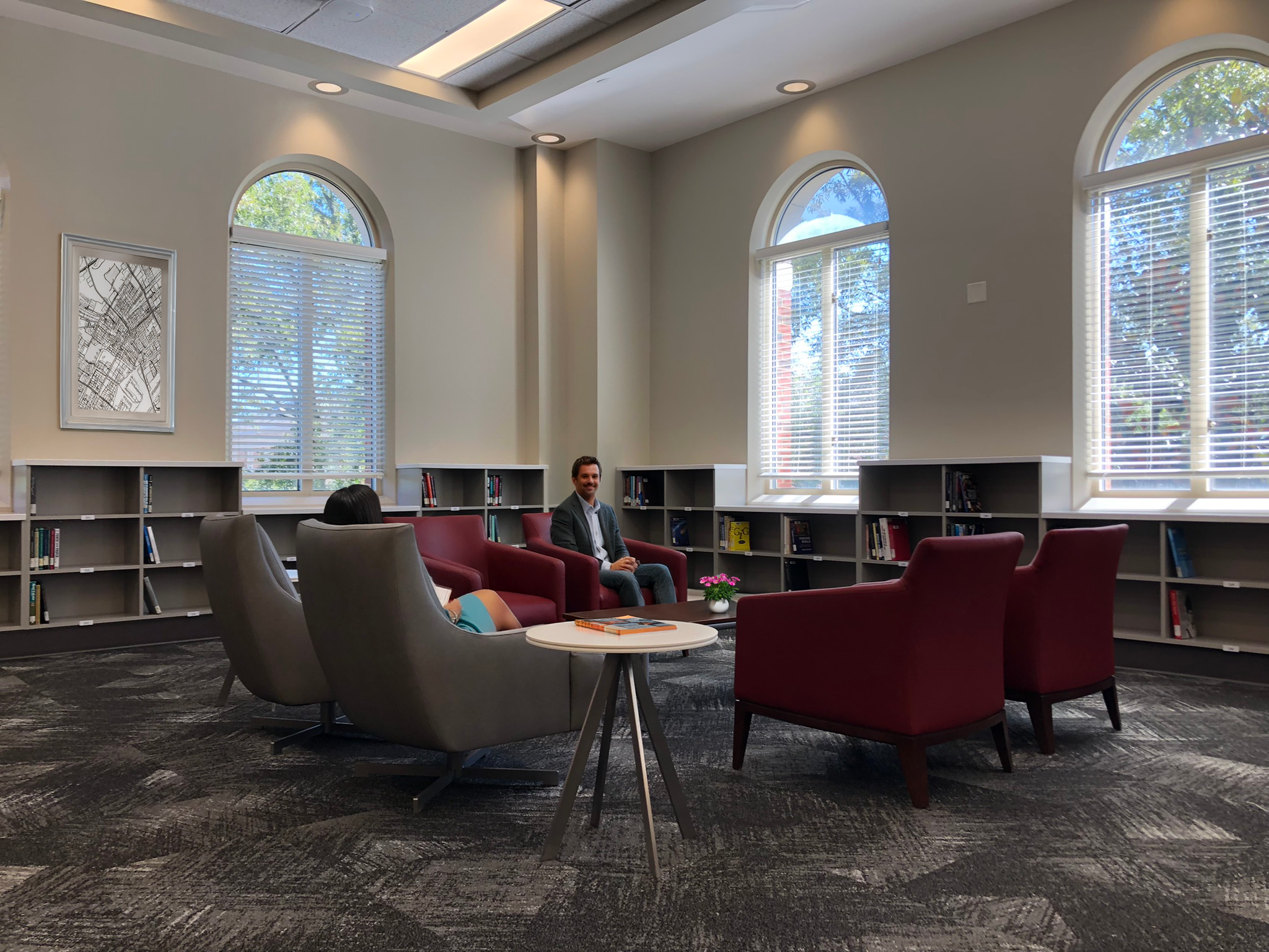 A modern library reading area with large arched windows, school colored upholstered seating, with natural light coming through the windows. - project by B Group Architecture, Inc