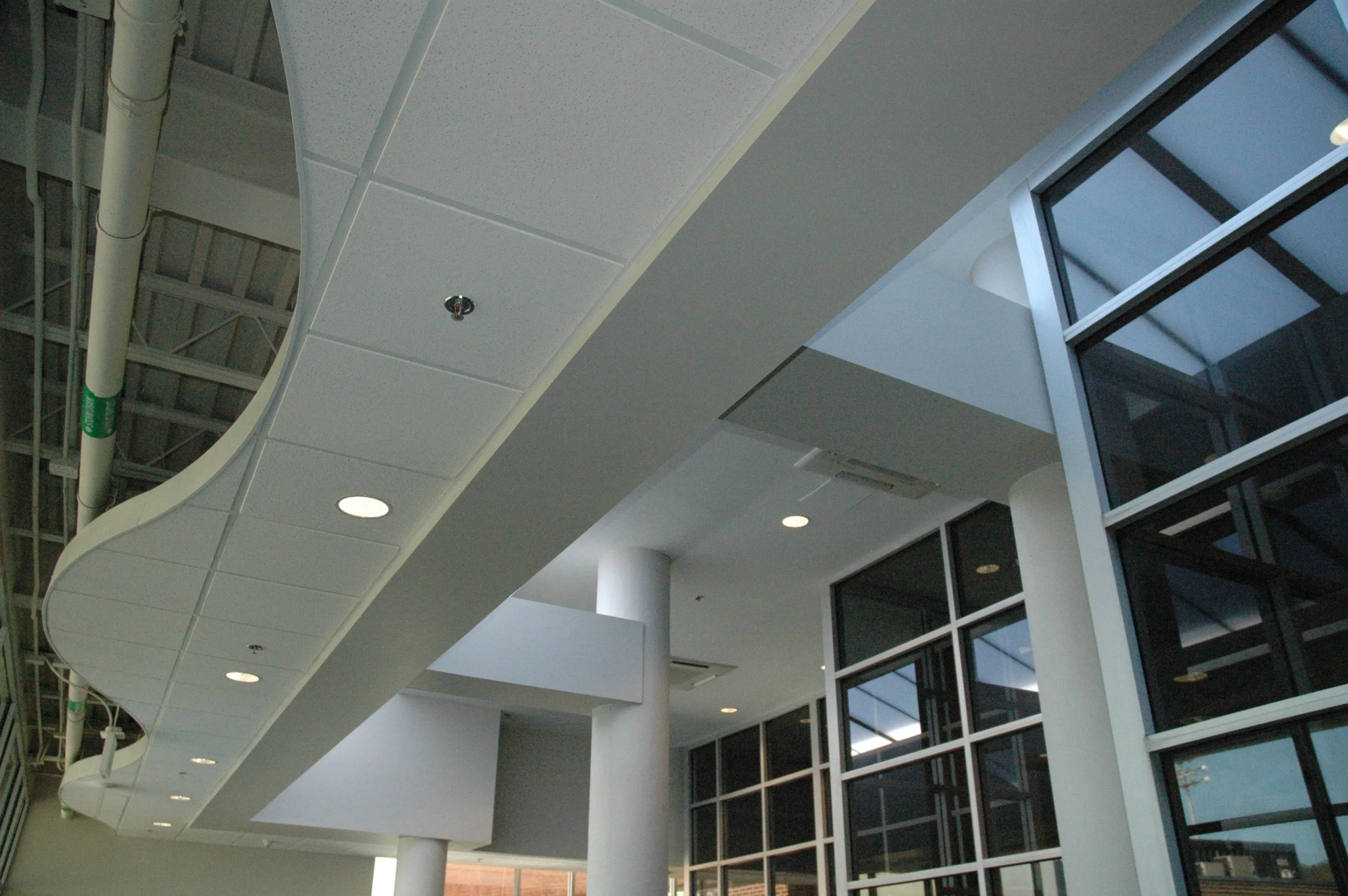 Interior view of a modern high school with large windows, wrapped columns and beams and exposed serpentined ceiling edge with exposed structure above.- project by B Group Architecture, Inc.