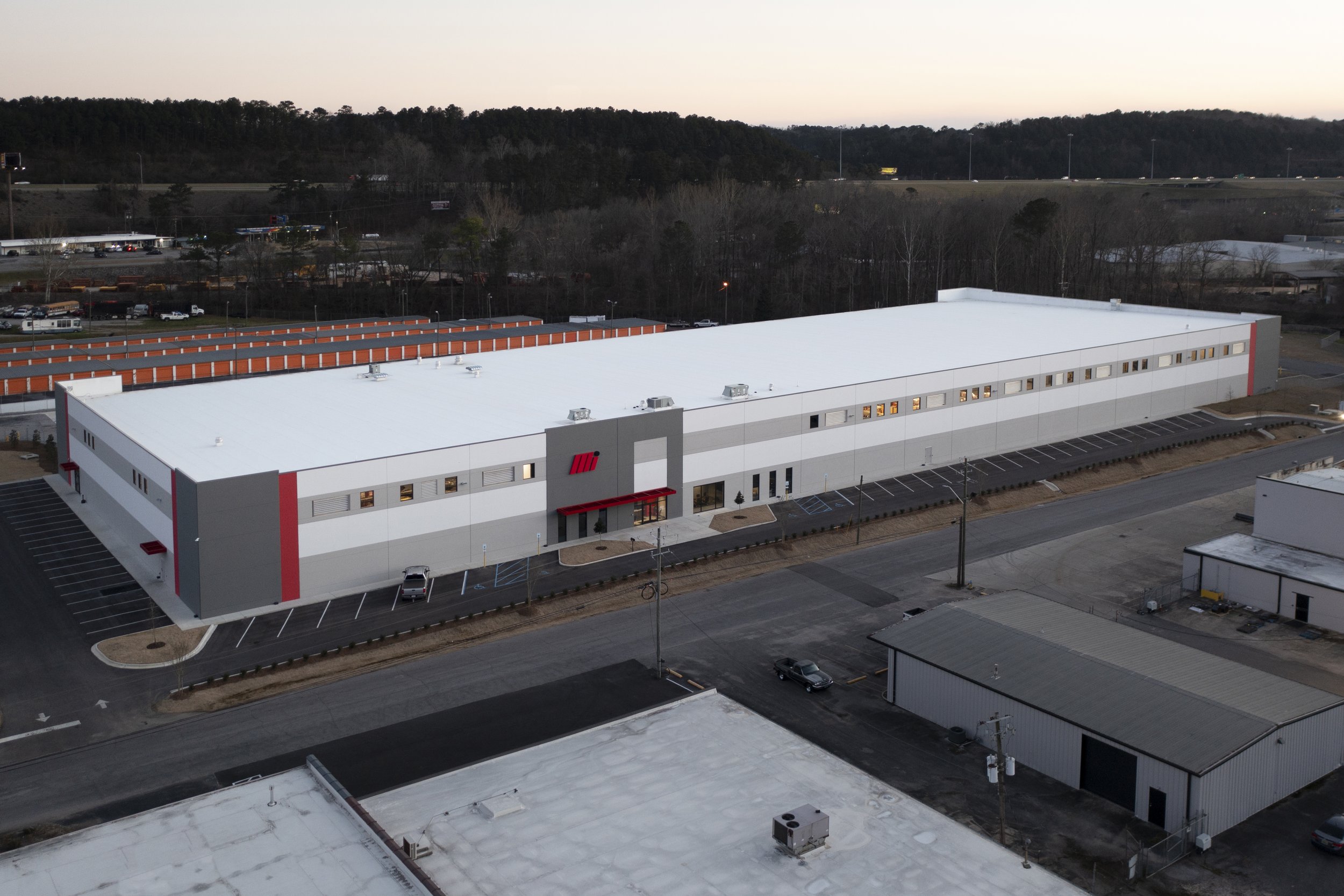 An exterior view of a modern building for Motion Industries Fluid Power Shop with their Mi logo on the wall, large glass doors at the entrance and tilt-up concrete construction. project by B Group Architecture, Inc.