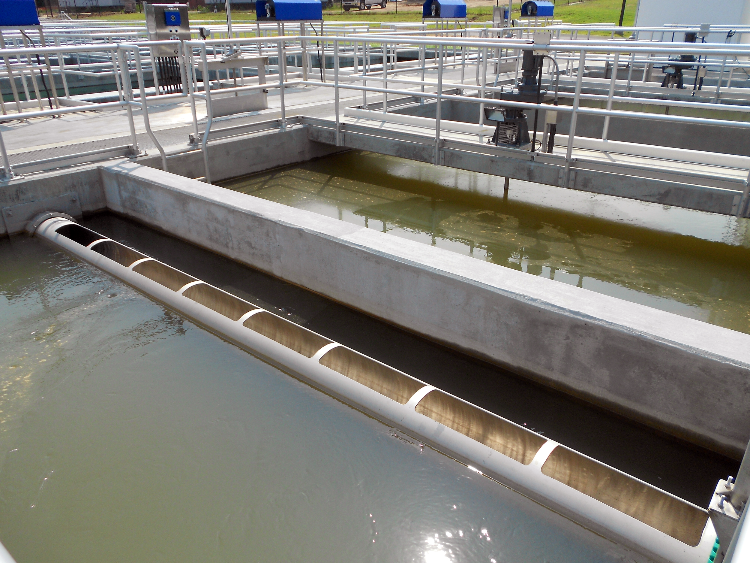 Multiple water treatment tanks with walkways and blue control boxes in an outdoor facility at Ft. Benning Water Treatment Plant - project by B Group Architecture, Inc.
