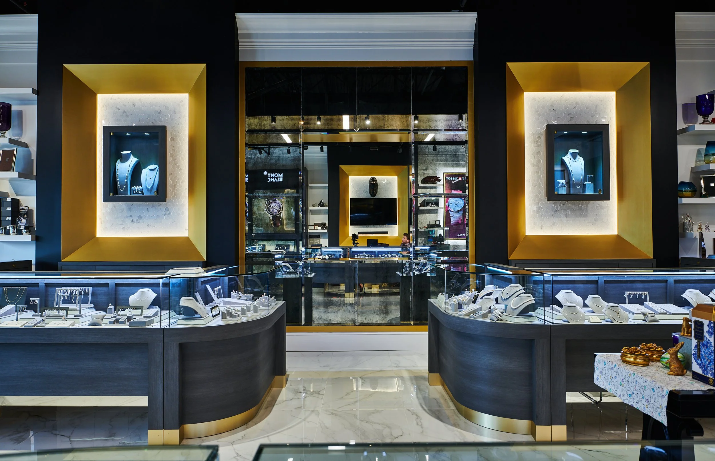 Interior of Barton Clay Fine Jewelers with display cases, shelves of jewelry, and an antiqued mirrored wall and marble accents. project by B Group Architecture, Inc 