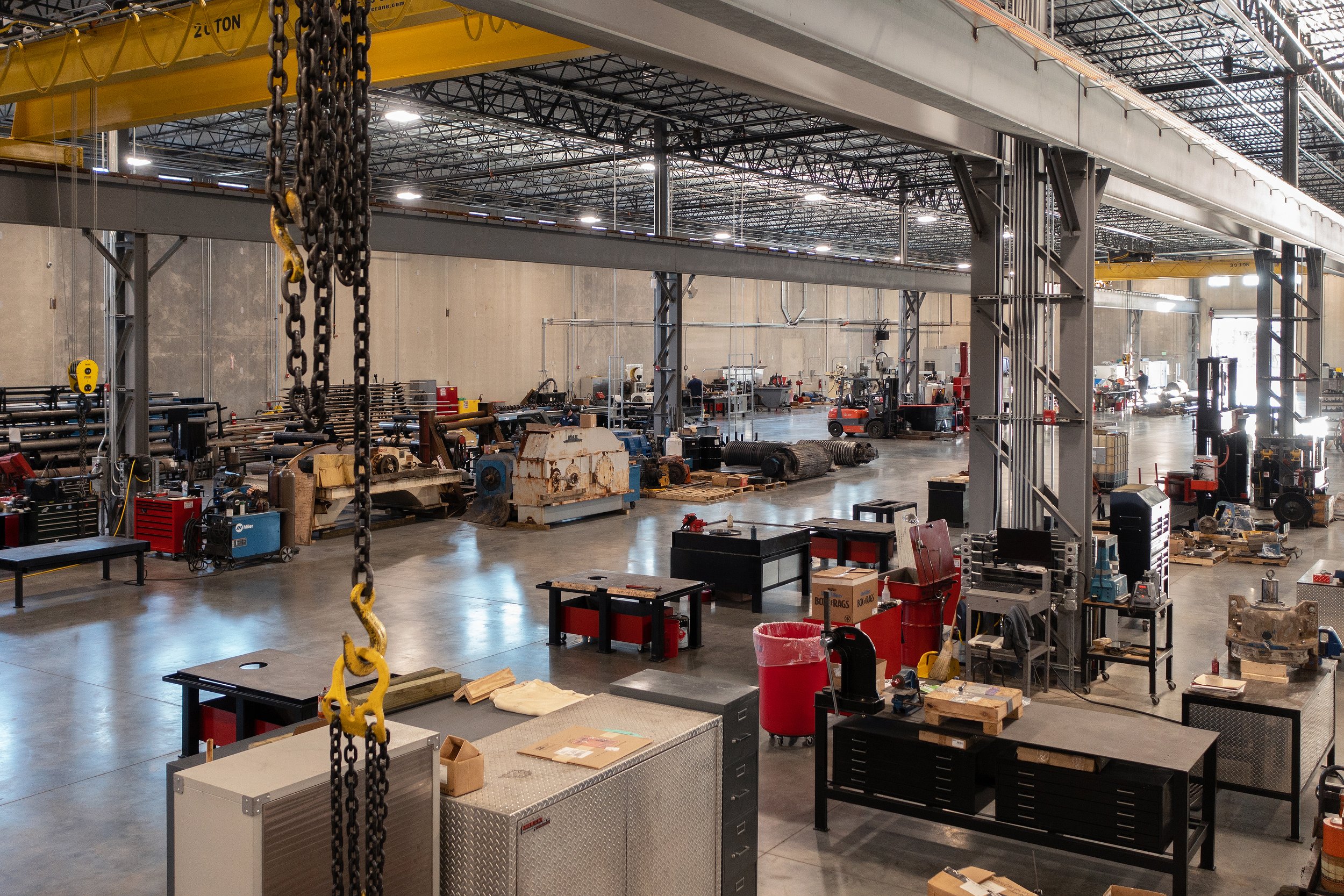 Motion Industries Fluid Power Shop  industrial warehouse with yellow overhead crane systems, construction equipment, and metal pipes on the floor. project by B Group Architecture, Inc.