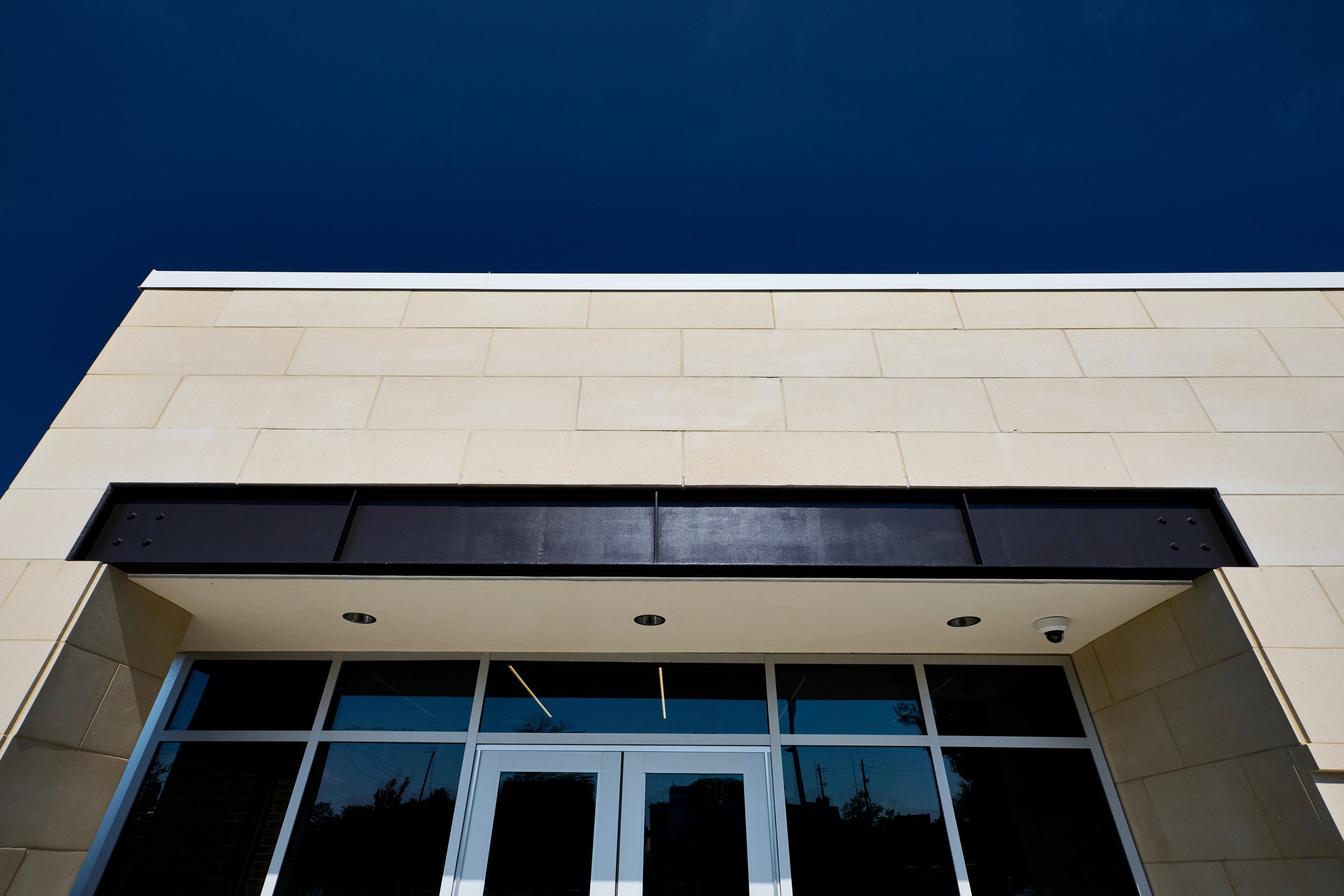 Front of a modern building with cast stone walls, glass doors, and steel lintel under a dark blue sky. -project by B Group Architecture, Inc.