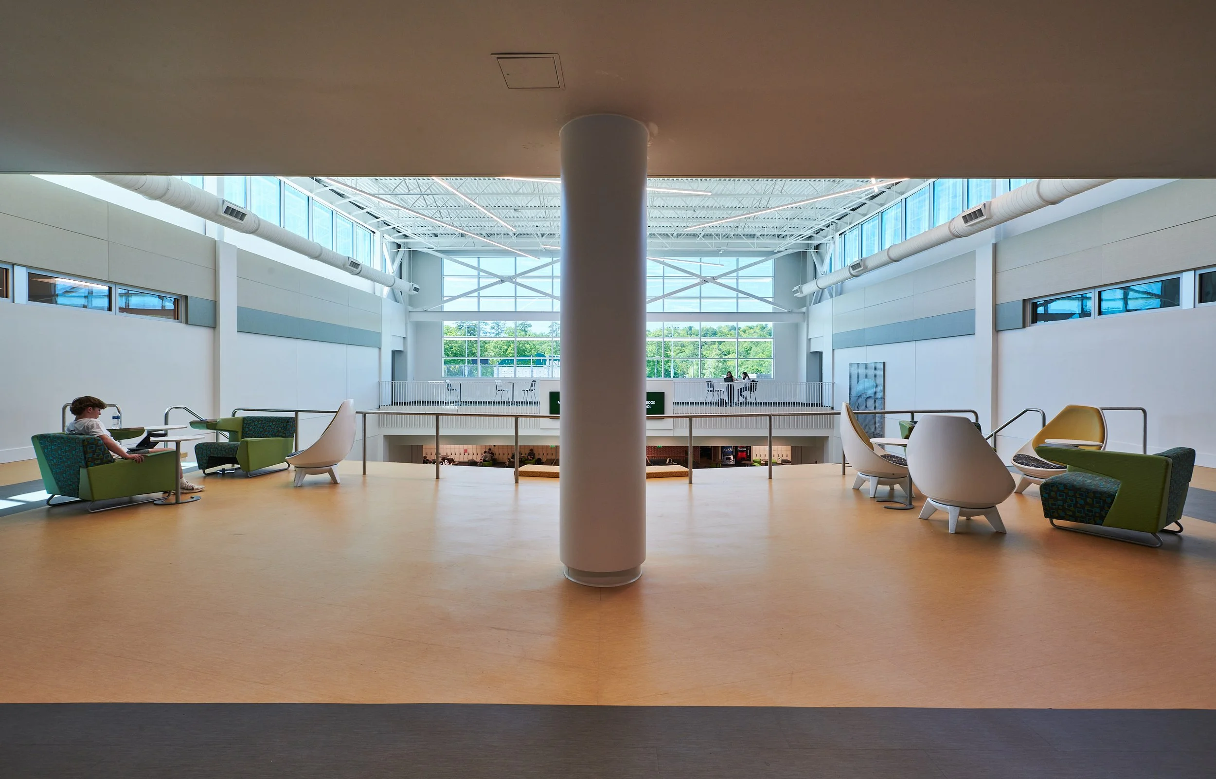 Modern indoor lounge area with armchairs and a child sitting on a chair, large windows, and a bright open space- project by B Group Architecture, Inc.