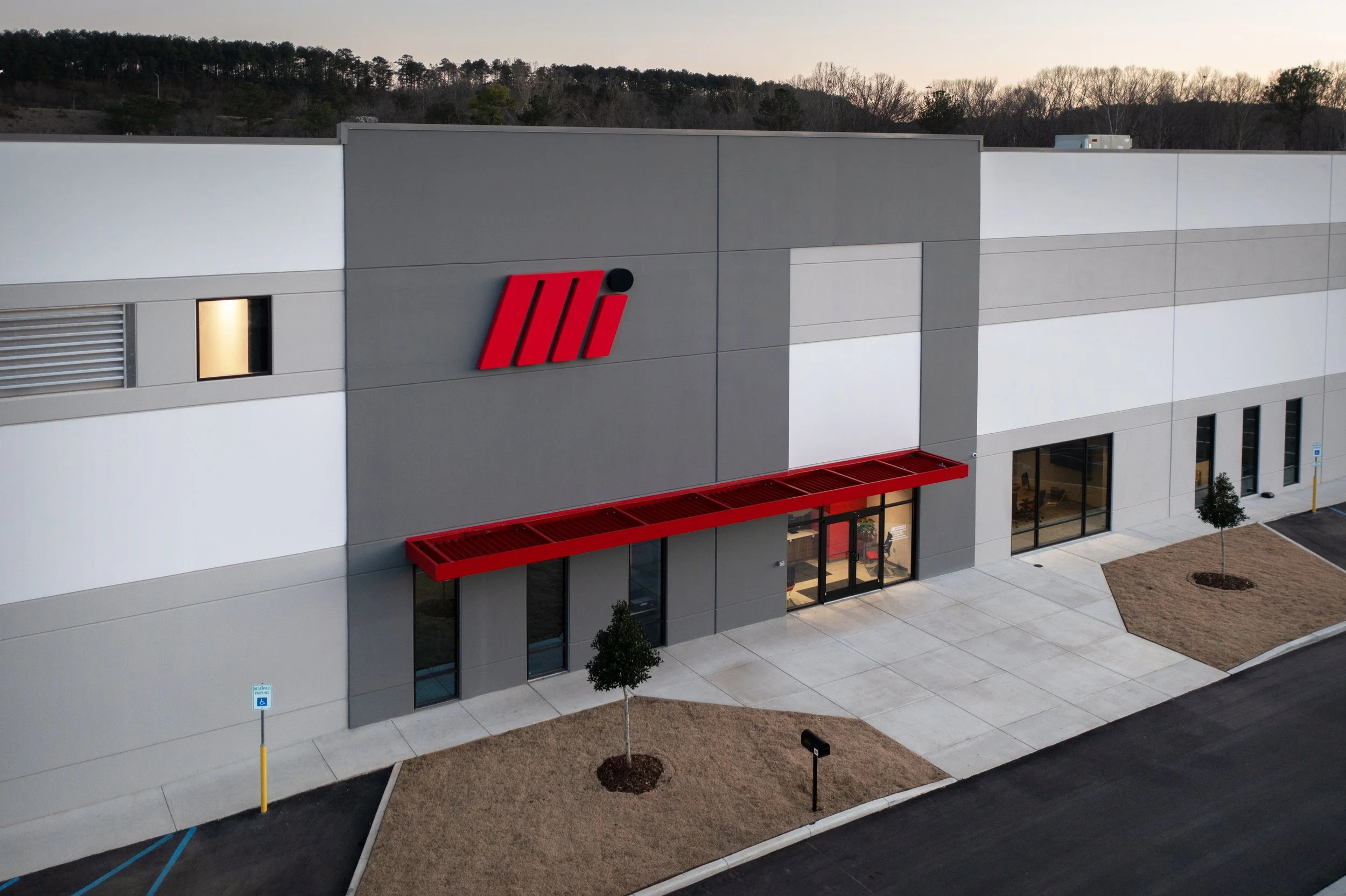 An exterior view of a modern building for Motion Industries Fluid Power Shop with their Mi logo on the wall, large glass doors at the entrance and tilt-up concrete construction. project by B Group Architecture, Inc.