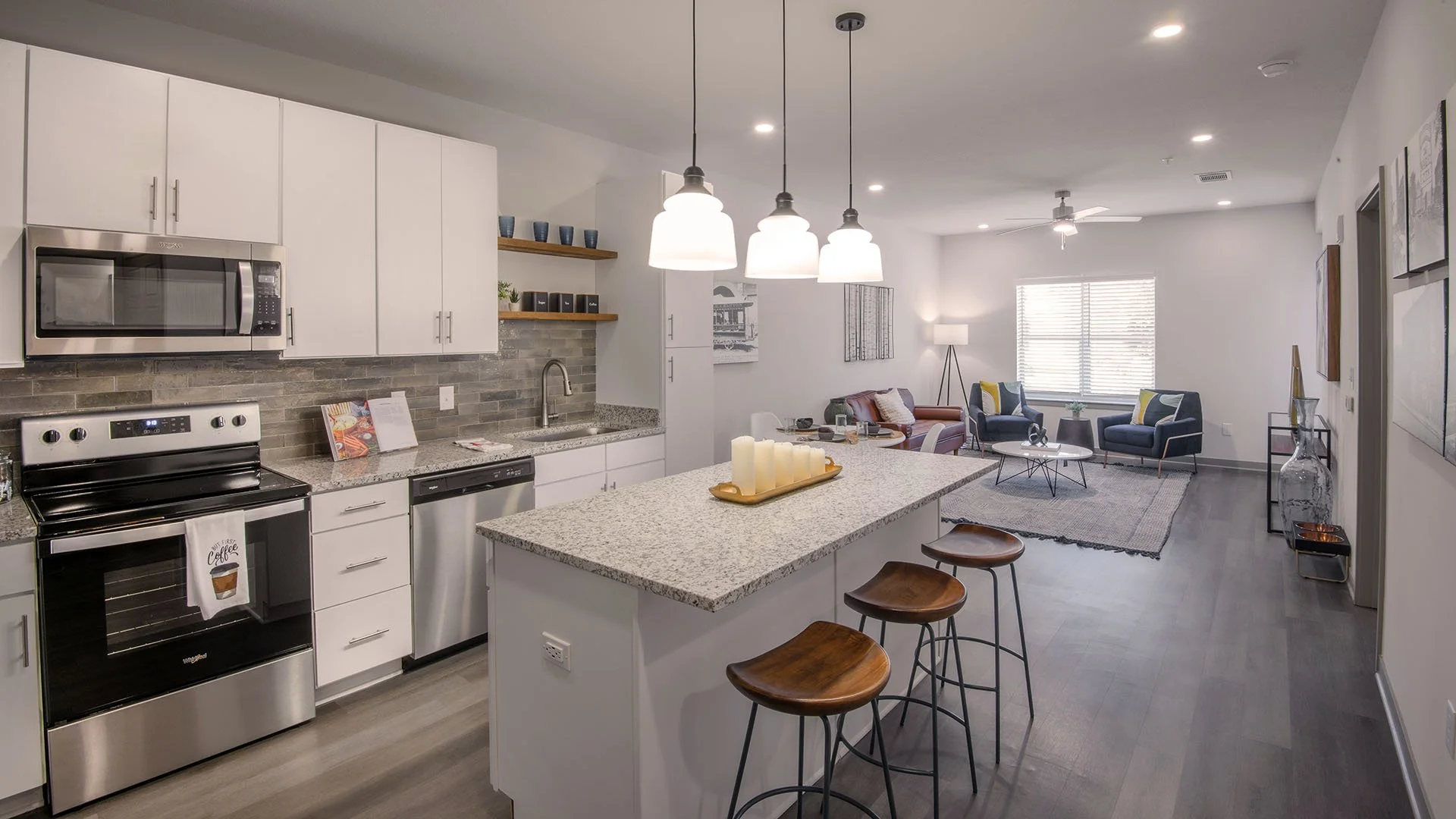 Open-concept kitchen with white cabinets, tiles backsplash, granite countertops, stainless steel appliances, and a kitchen island opening up to a living room in this one bedroom apartment. - project by B Group Architecture, Inc..