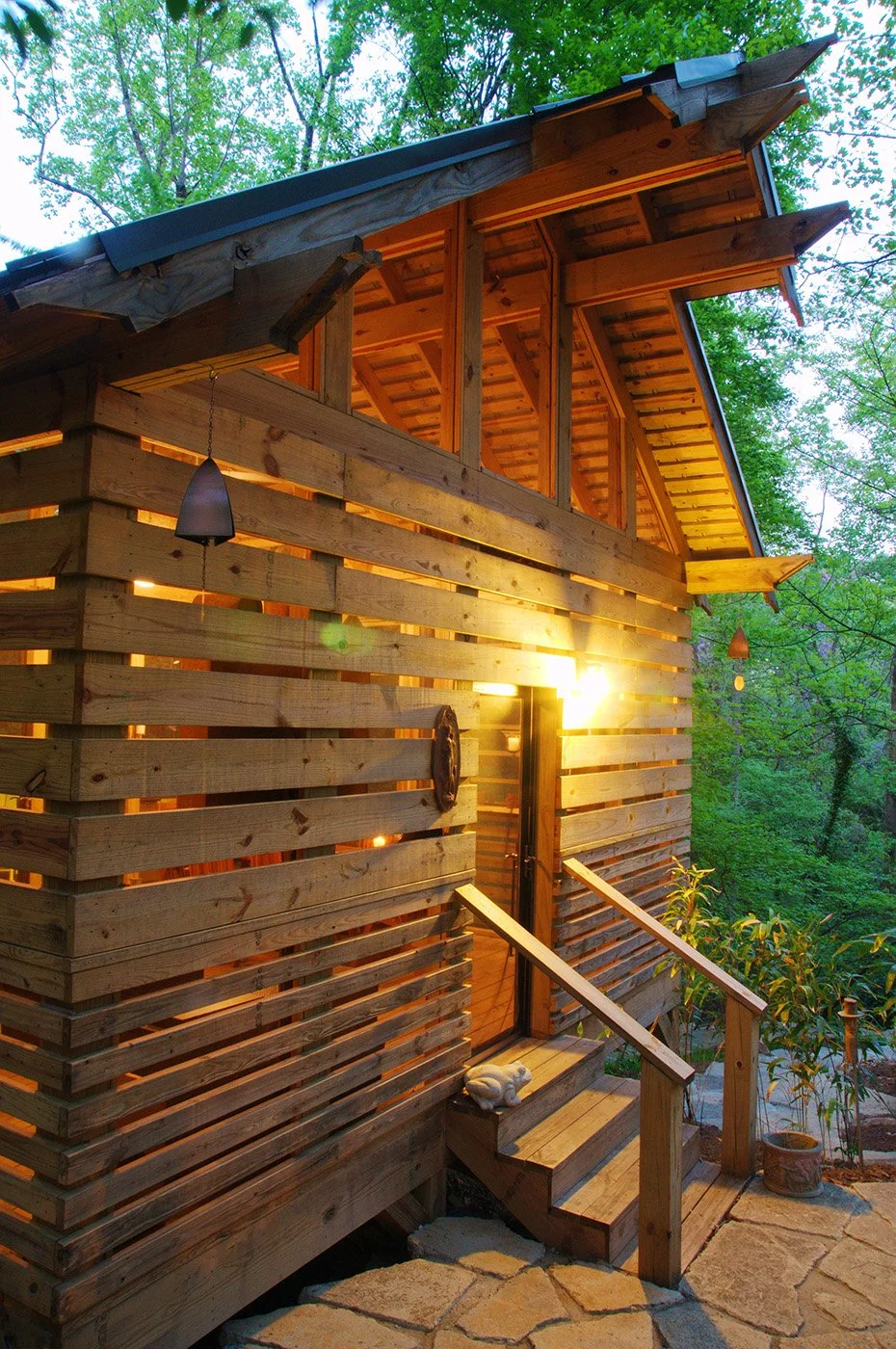Creekside Pavilion with slat wall design located in a lush green forest, illuminated from inside. project by B Group Architecture, Inc.