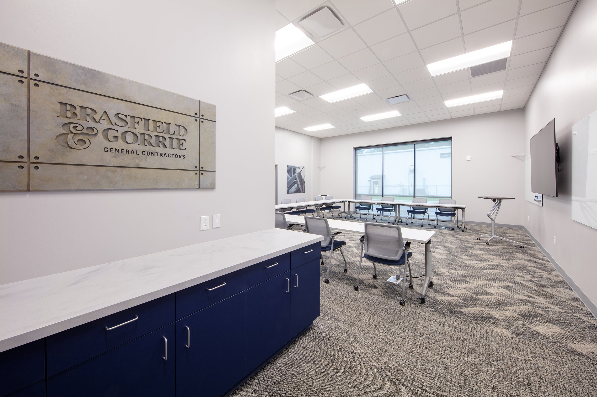 Training classroom with chairs, tables, a mounted TV, large window, and a sign for Brasfield & Gorrie General Contractors.