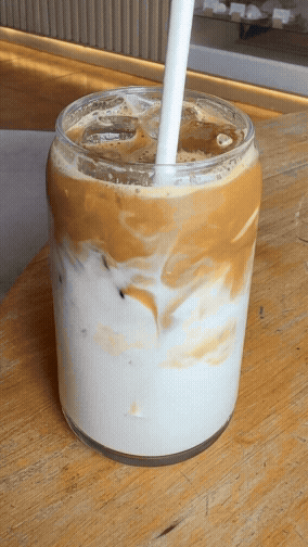 Glass of iced coffee with milk and a straw on a wooden table.