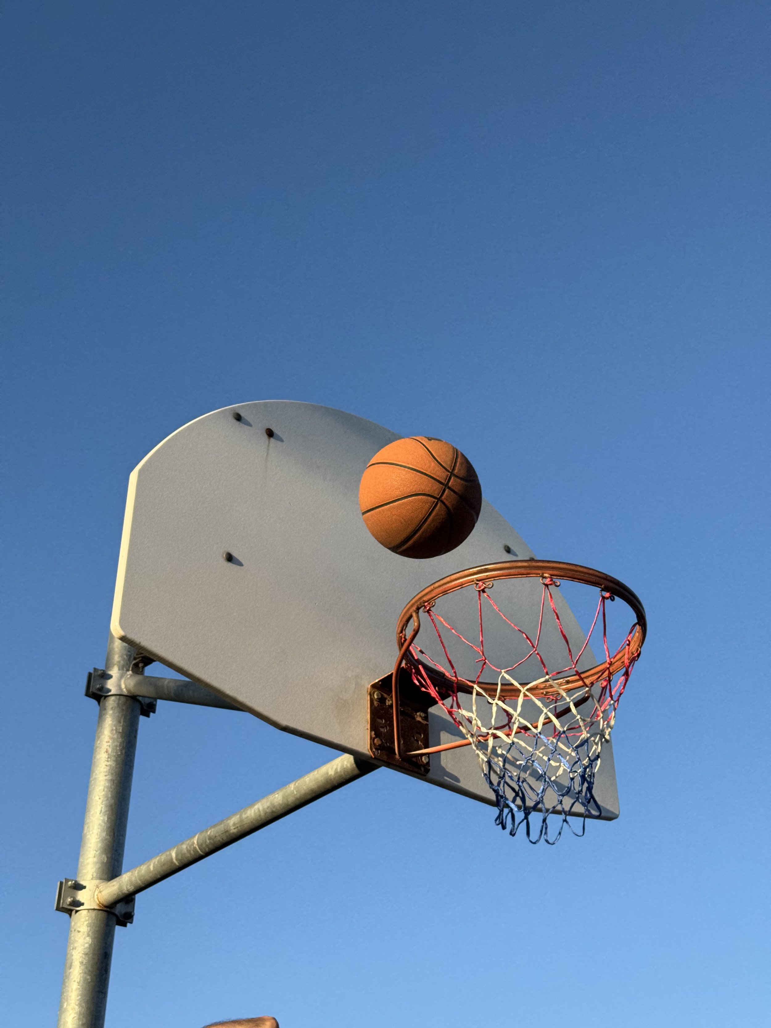 Basketball hoop with a basketball about to go through the net against a clear blue sky.