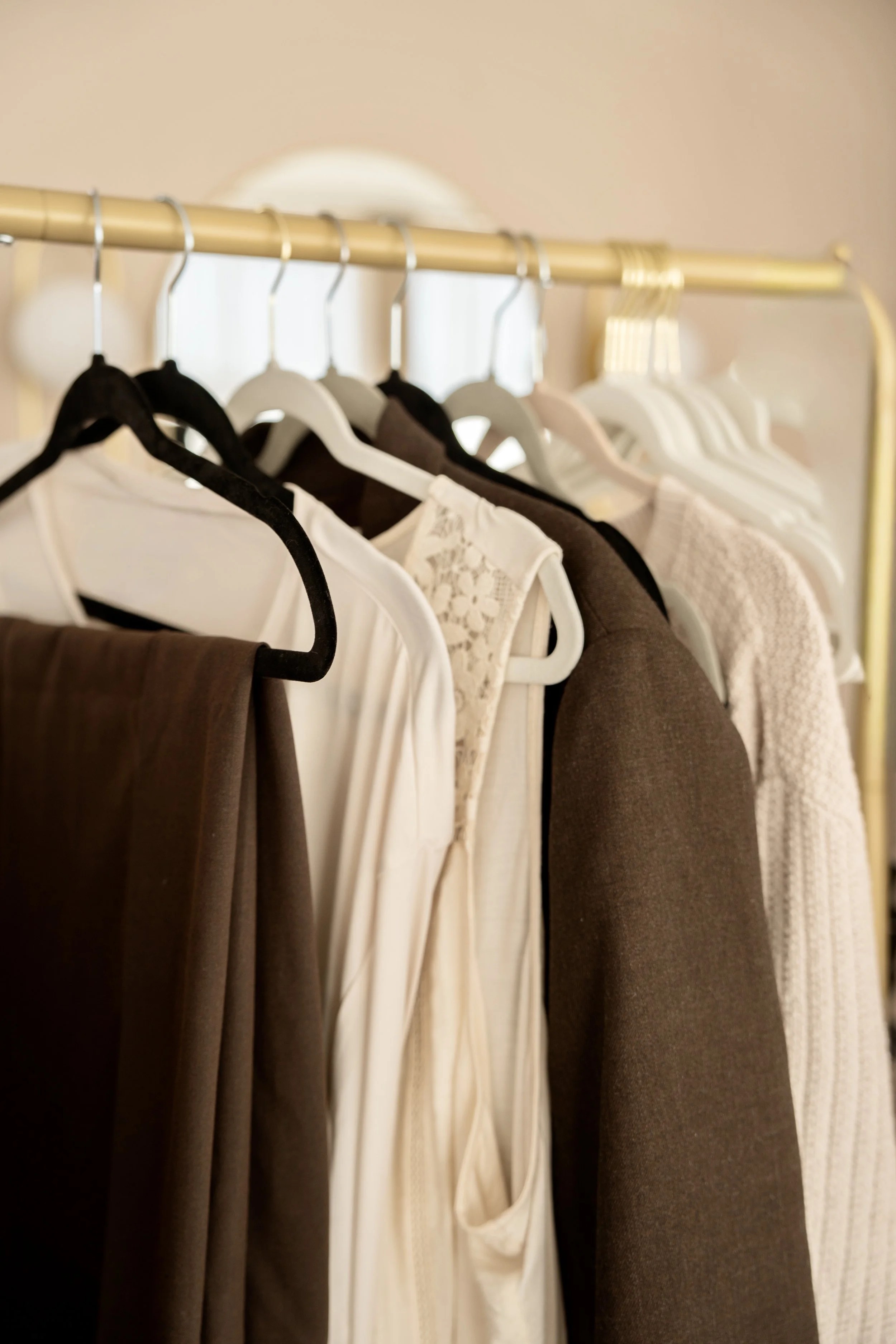 Clothes hanging on a gold clothing rack, including white, beige, brown, and black garments.