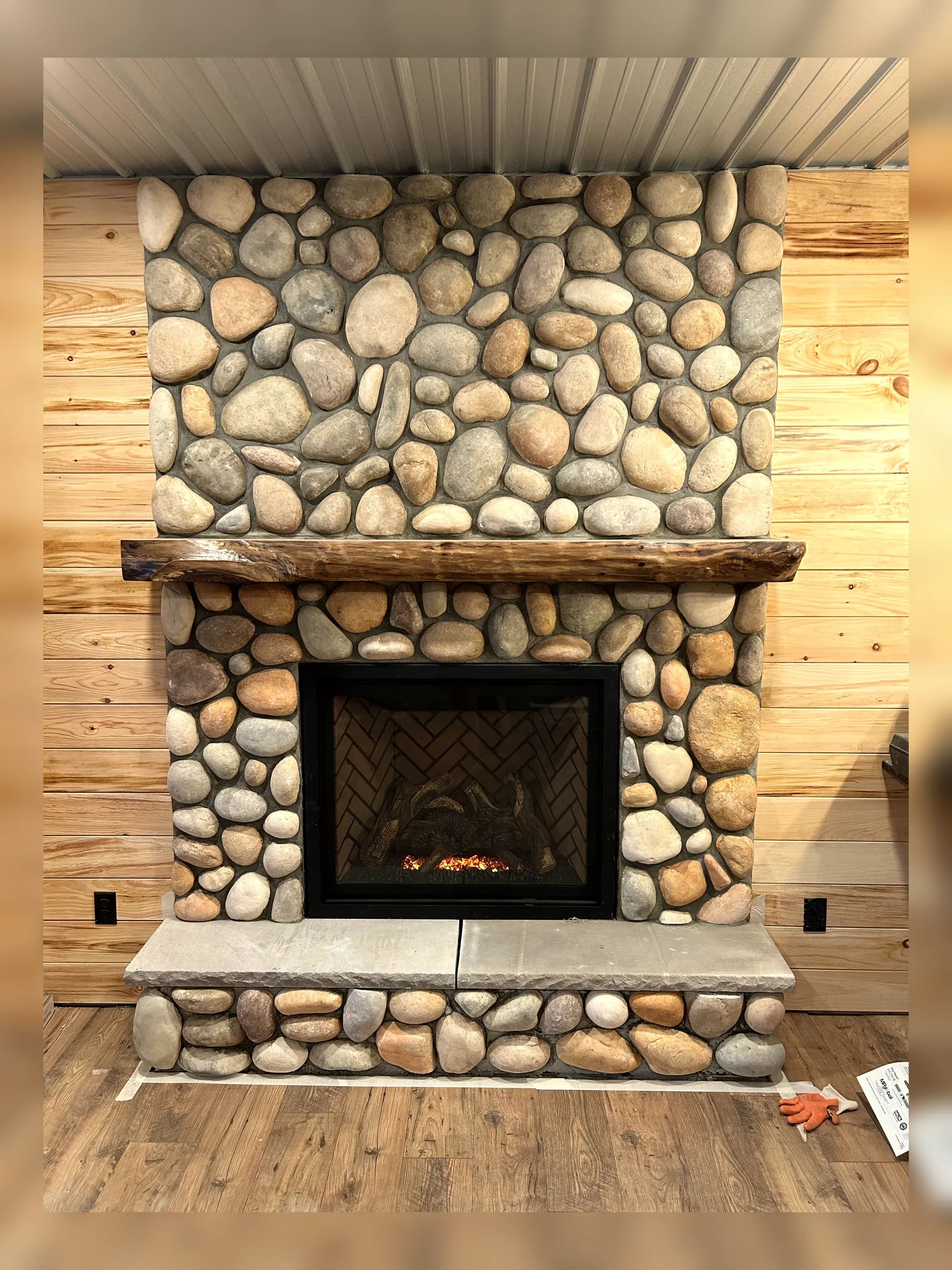 A stone fireplace with a wooden mantel, set against wooden wall paneling, with a small fire burning inside.