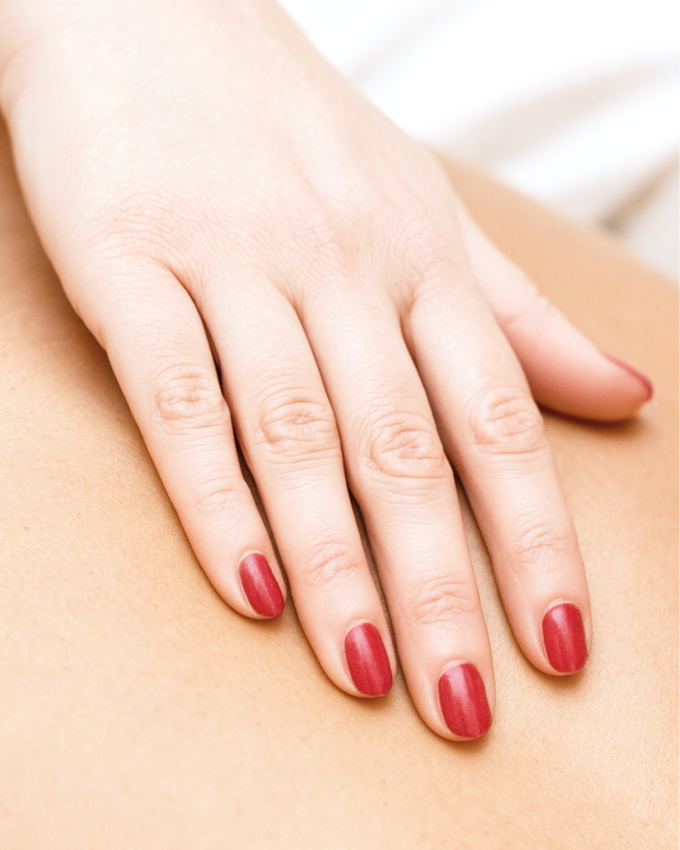 Close-up of a woman's hand with red painted nails resting on skin.