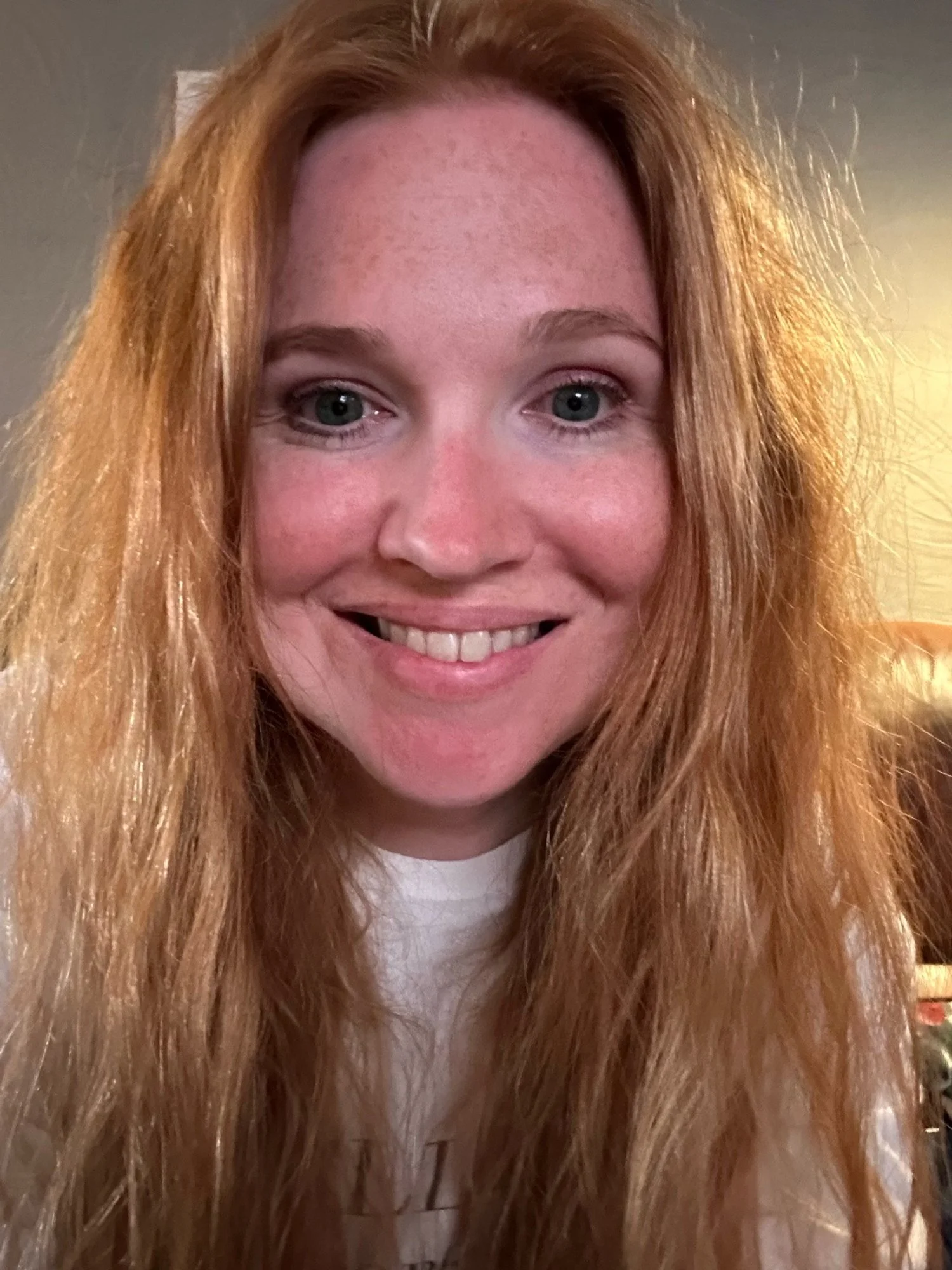 A young woman with long, curly red hair smiling at the camera.