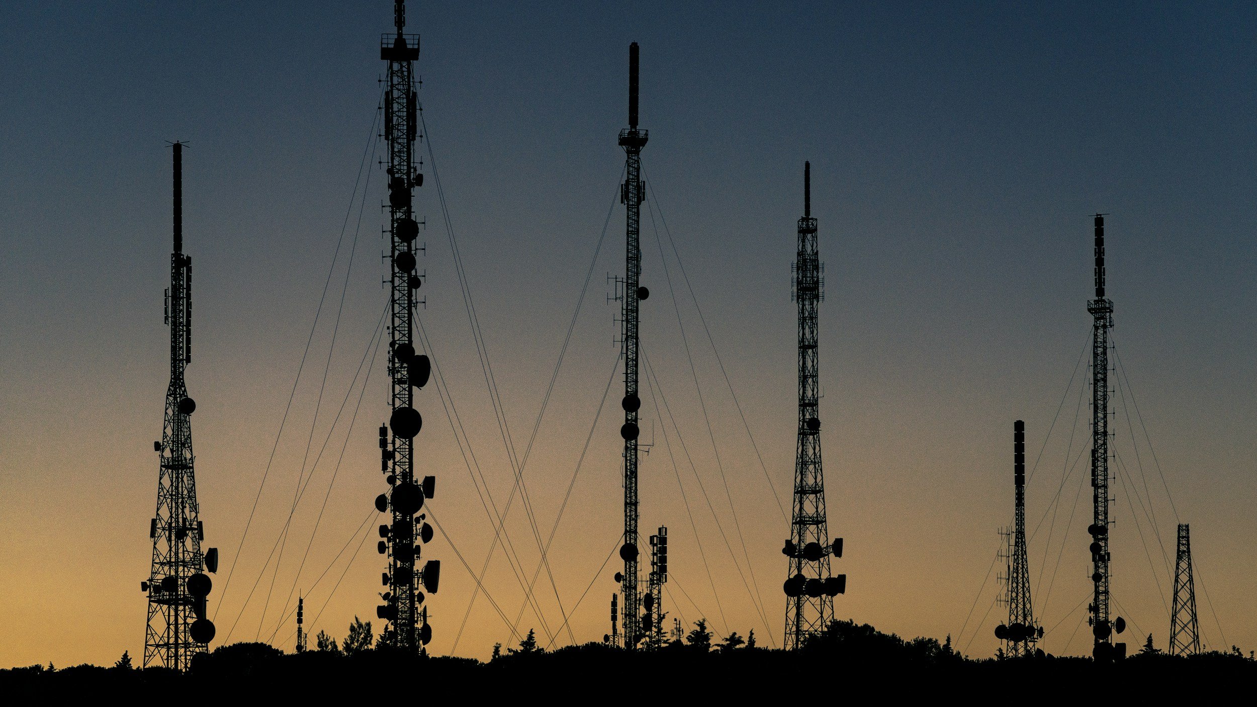 Silhouettes of multiple communication towers against a sunset sky.