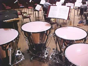 A view from a set of timpani looking out at a concert hall with musicians and music stands.