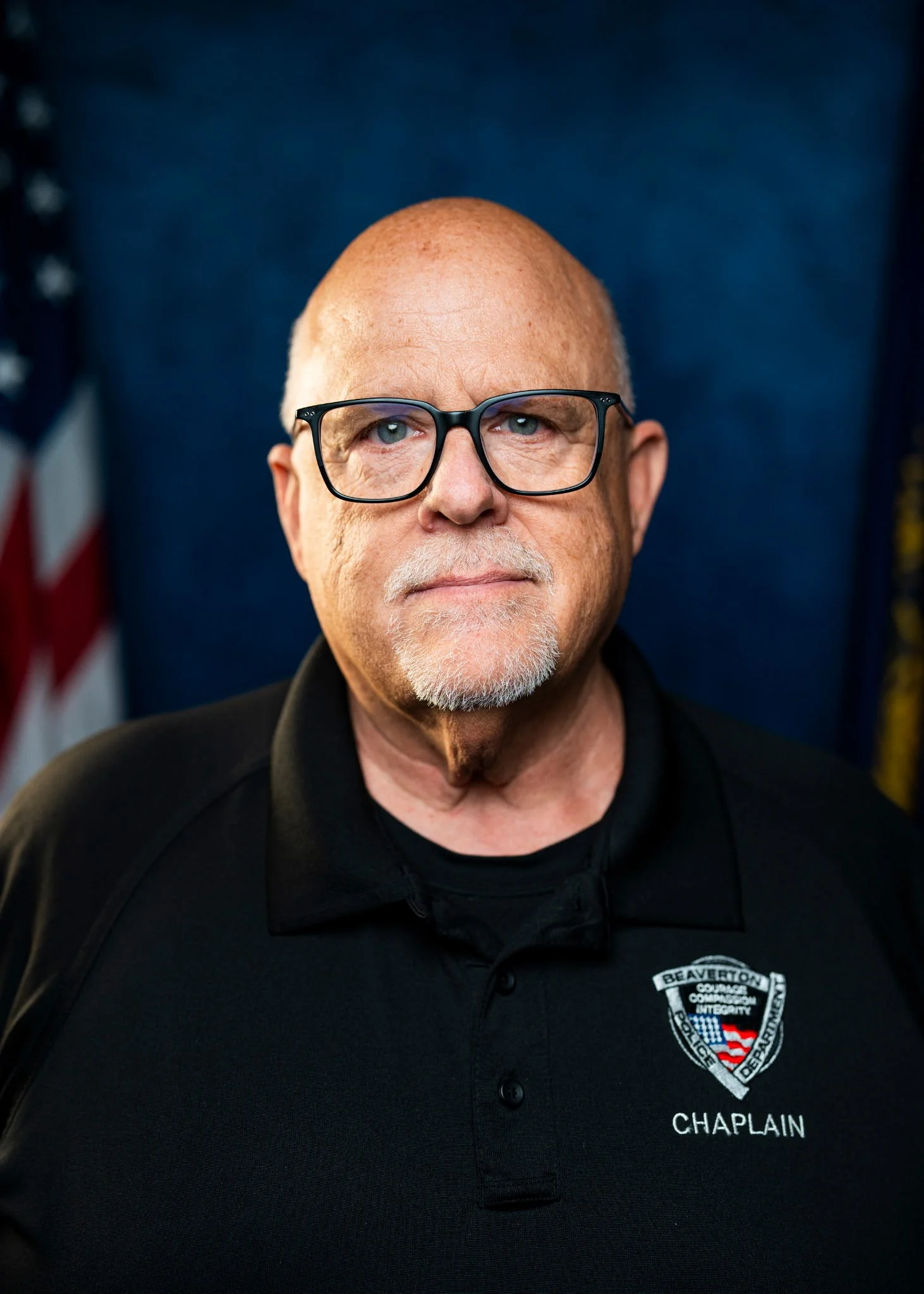 A smiling middle-aged man with glasses and a beard, standing outdoors in front of a tree.