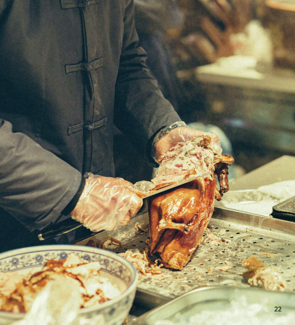 Person slicing a roasted turkey in a kitchen or deli setting, wearing black gloves and coat, with bowls and utensils nearby.