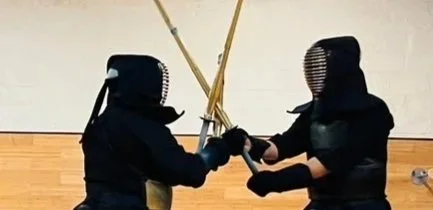 Two people dressed in kendo gear practicing sword fighting in a dojo.
