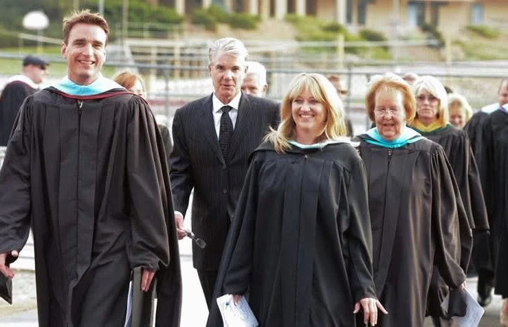 Cali in a graduate gown with other adults surrounding.