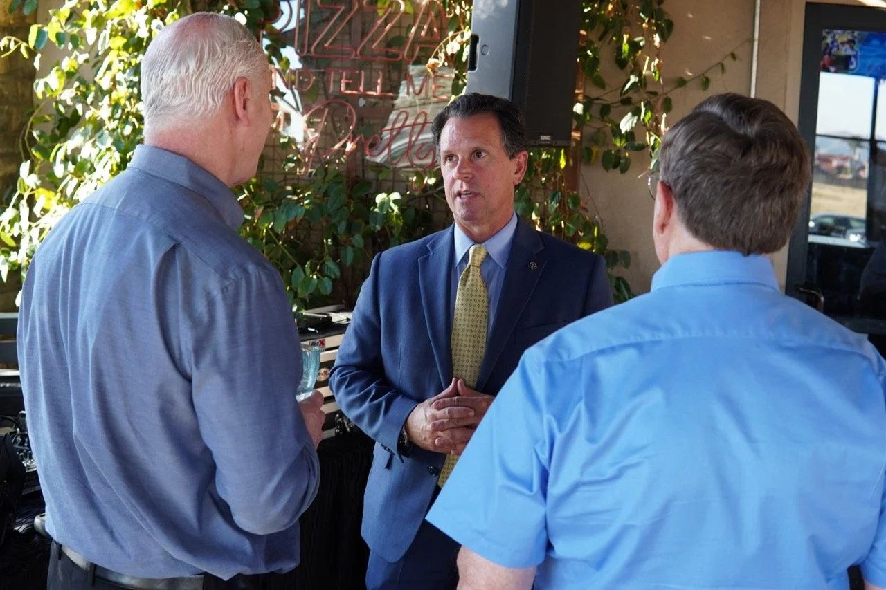 District Attorney Jason Anderson, Cali Bink's husband and a community member having a conversation at the event. Jason is facing the camera.