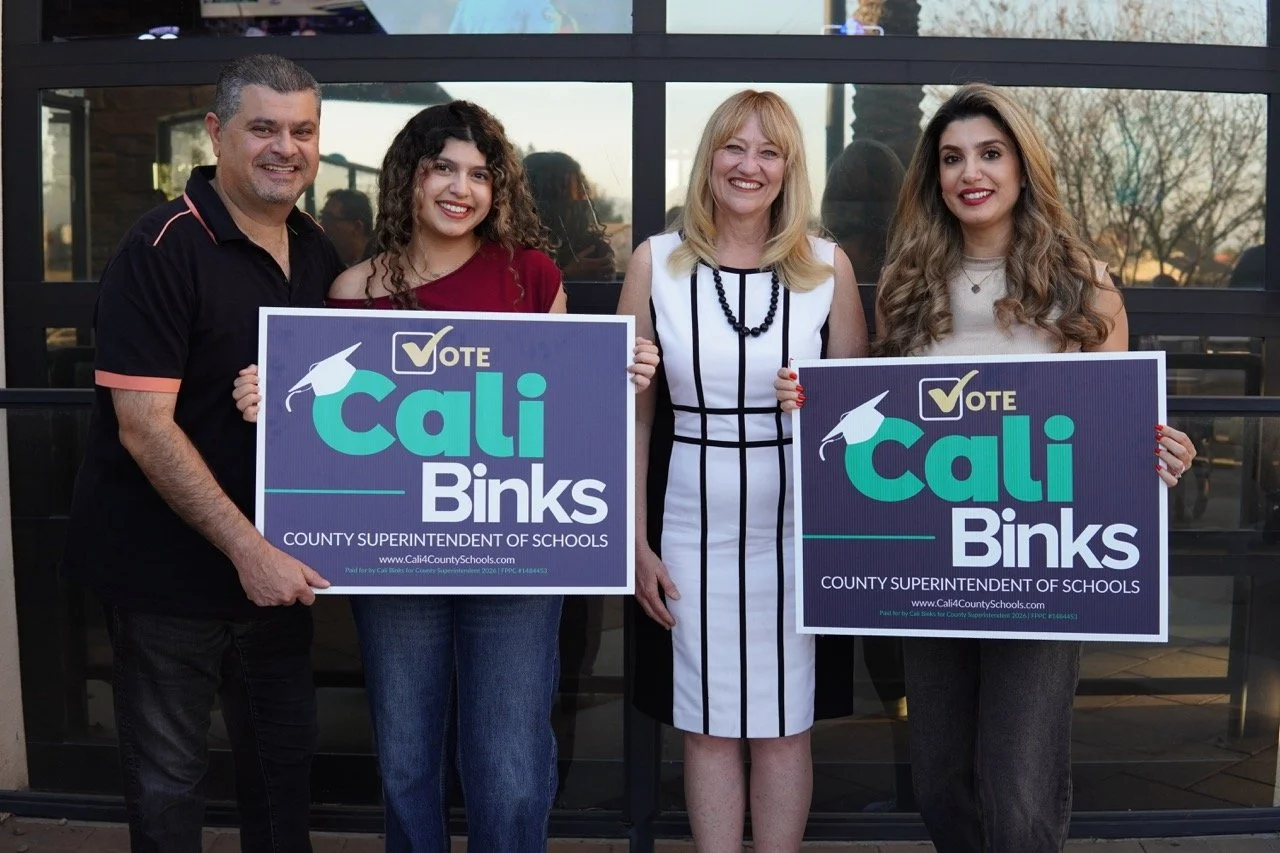 Cali posing with yard signs with a father, mother, and former student of Los Osos High School.