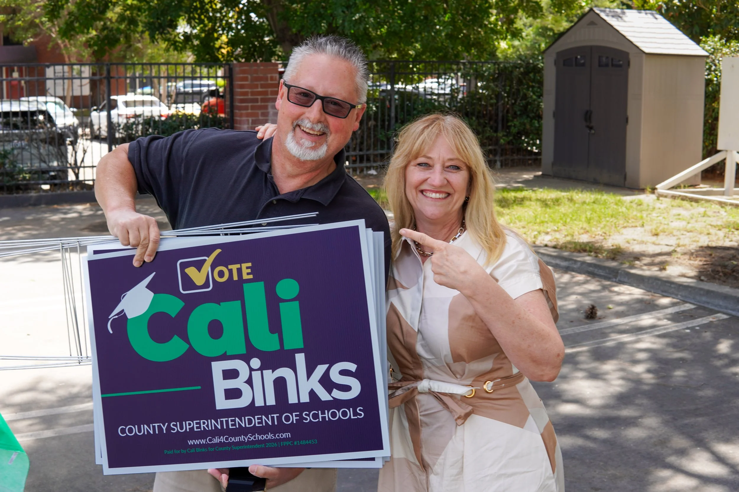 Adult holding a Cali Binks campaign sign next to Cali pointing to the yard sign.