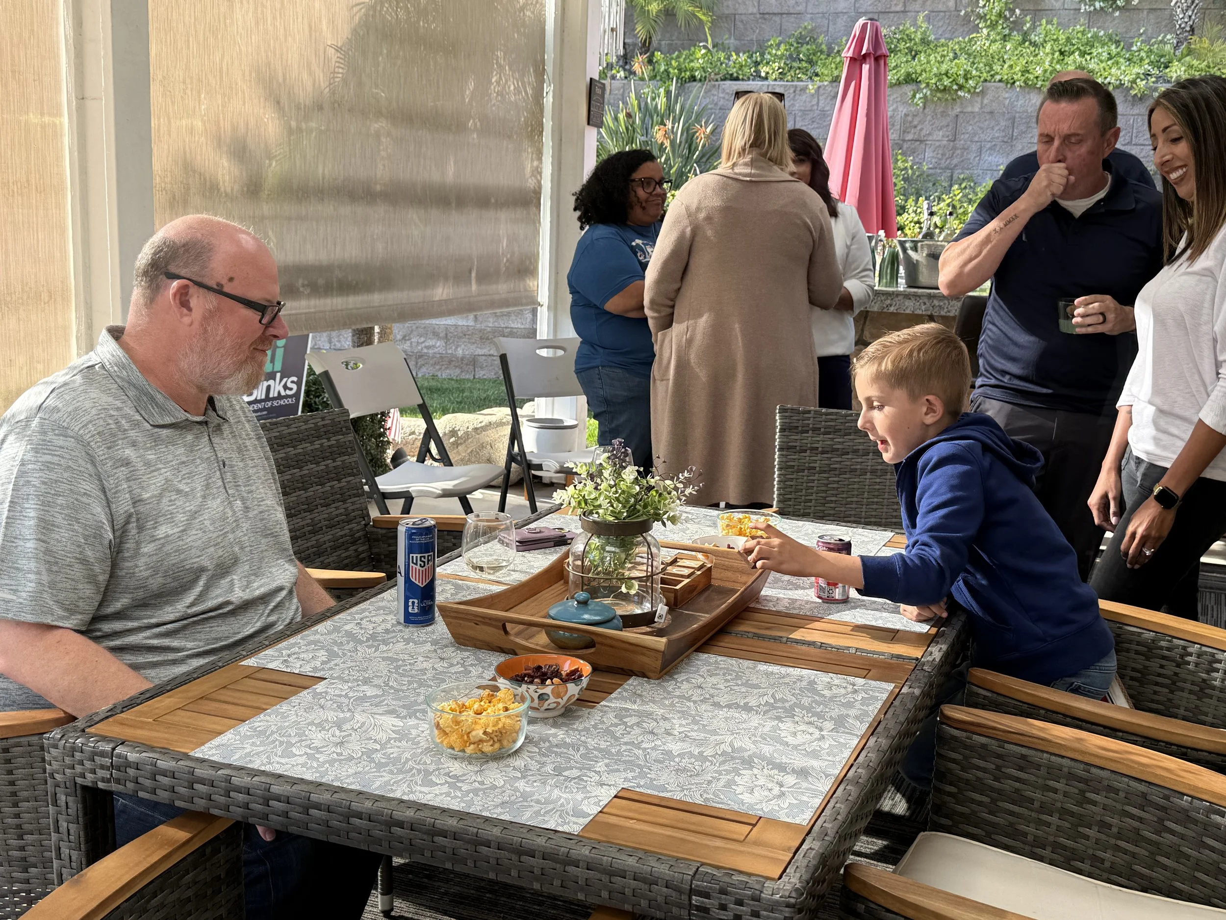 An adult playing a board game with an elementary student, parents watching behind him and next to them a crowd of community members