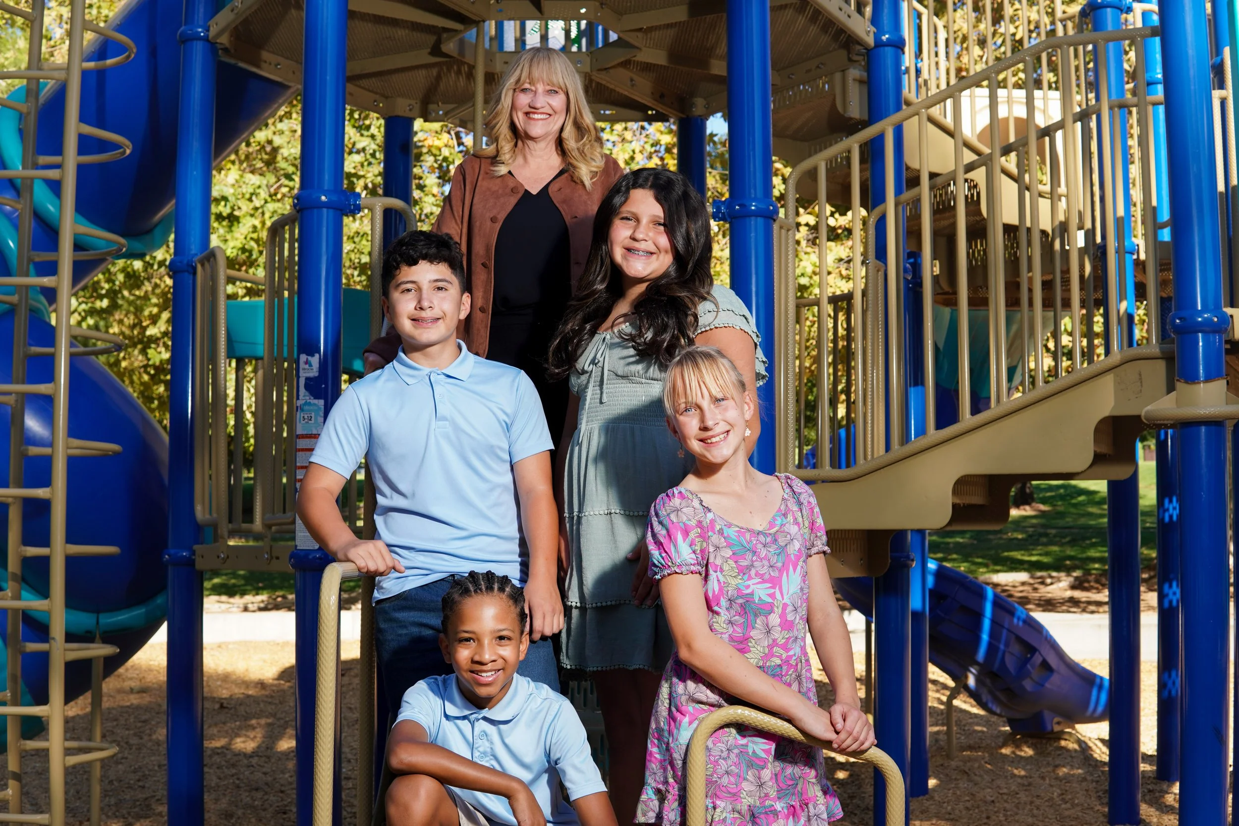 Cali with four students posing in front of a playground structure.