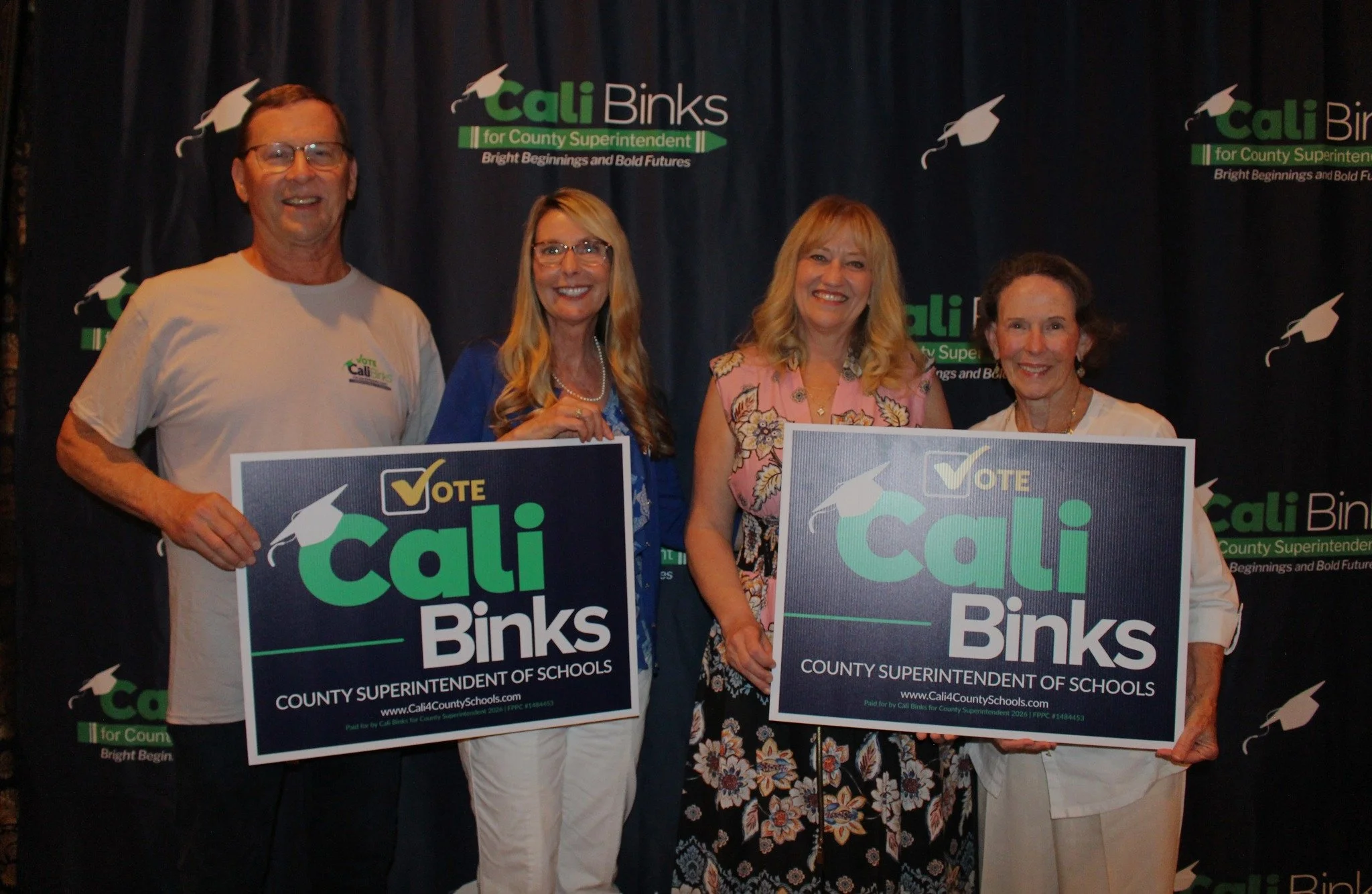 Cali Binks with three guests holding a yard sign promoting her campaign.