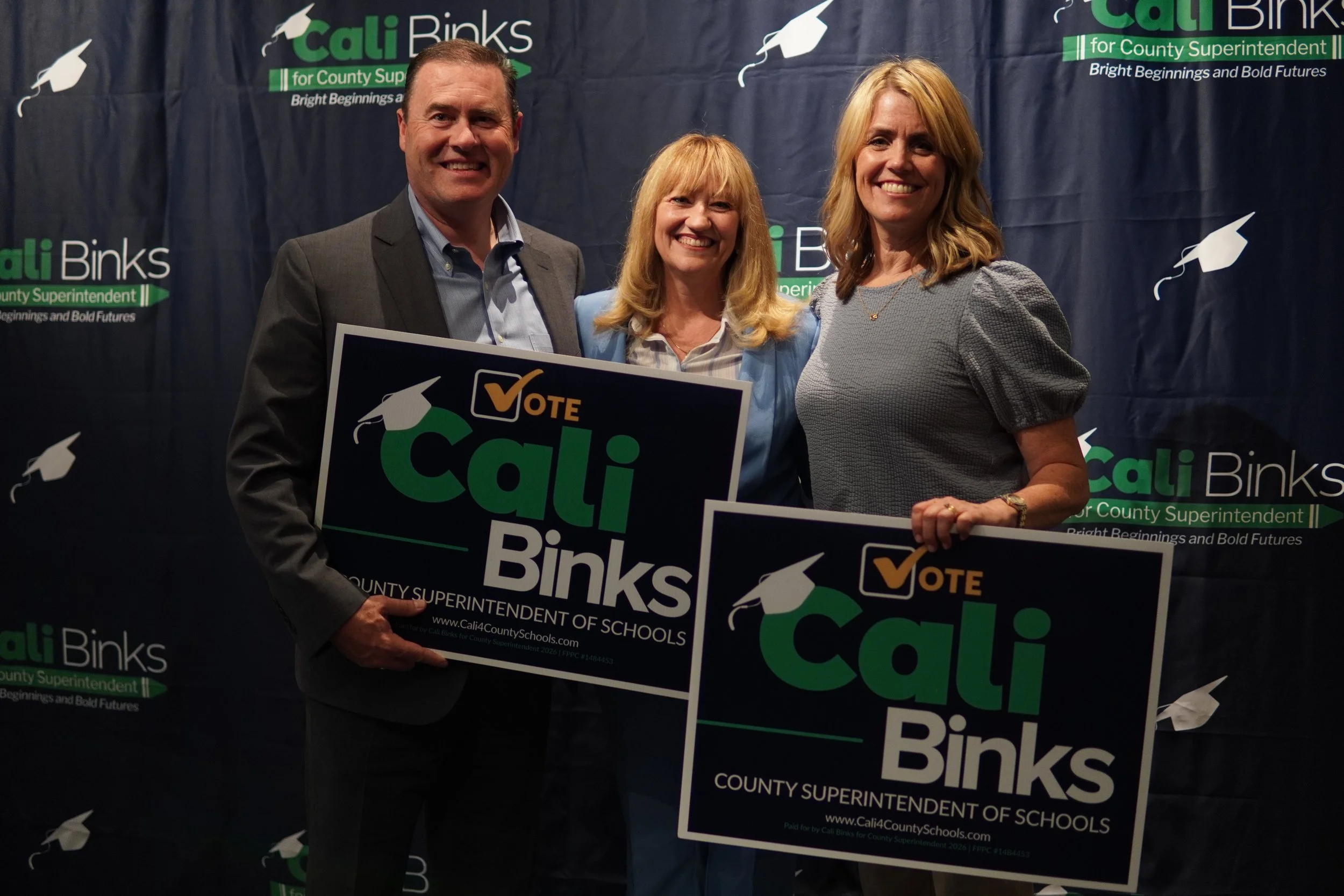 Two adults with yard signs with Cali