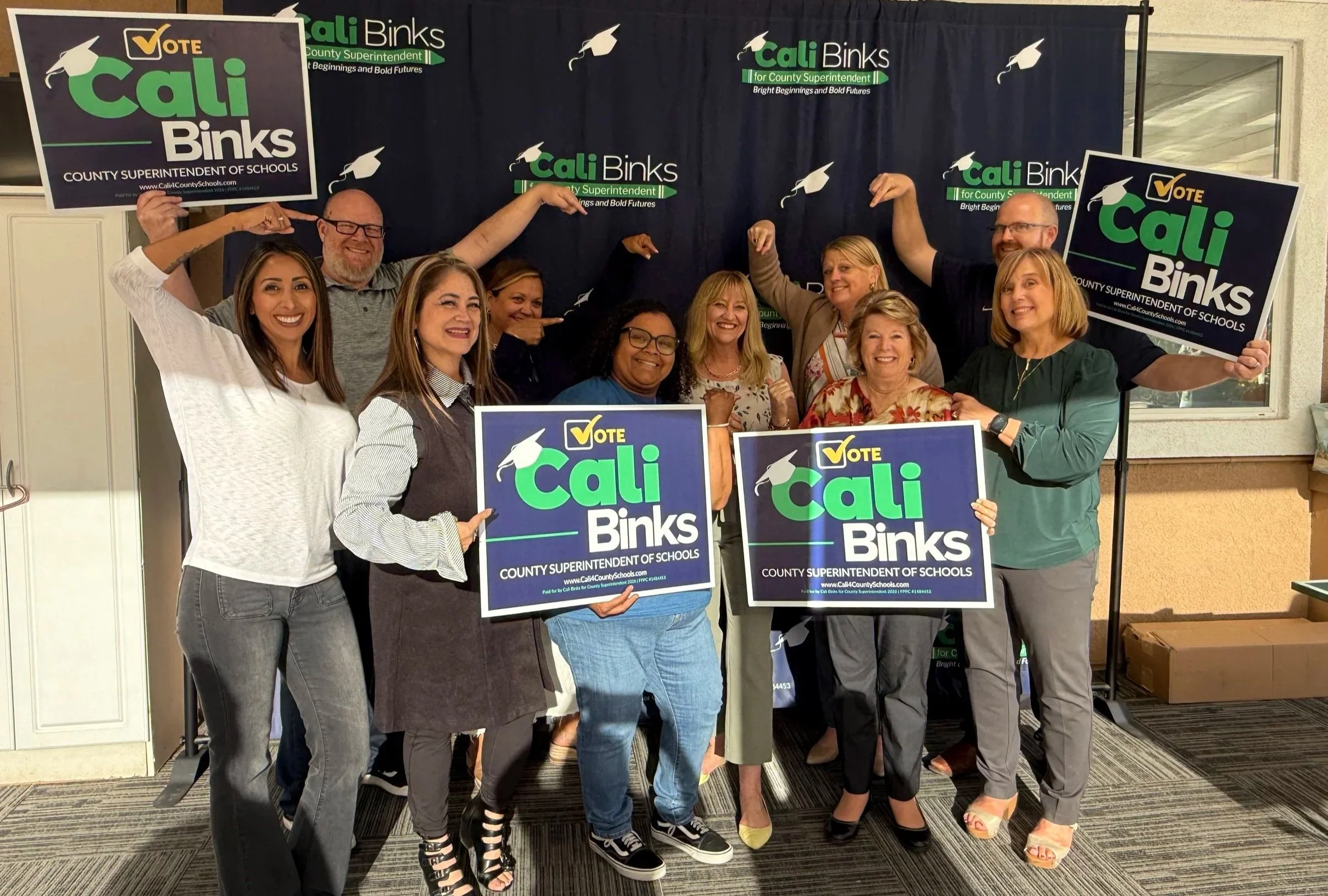 Group of community members holding yard signs and pointing at Cali.