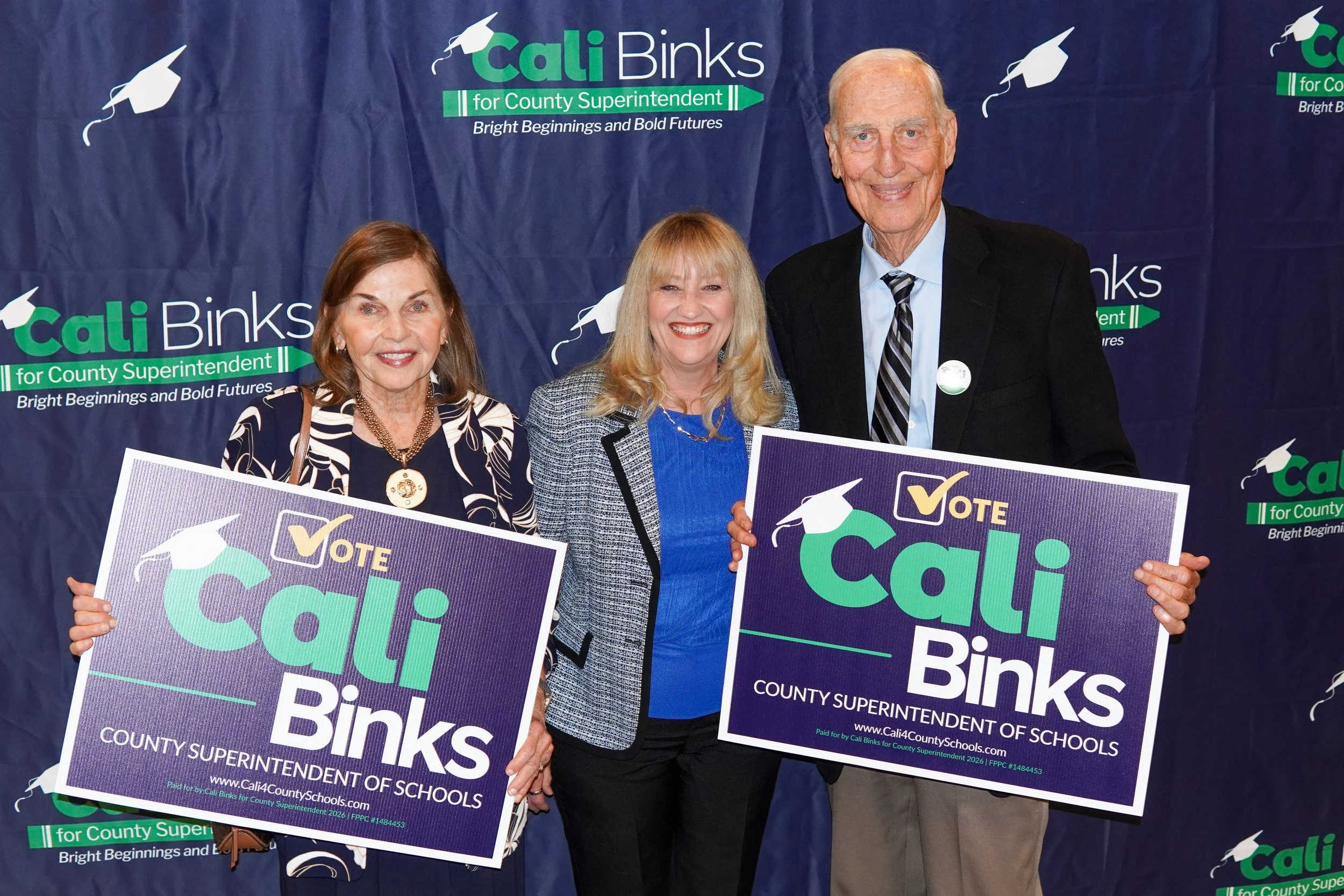 Cali posing for a photo with Dr. Cheryl and Herb Fischer holding yard signs. 