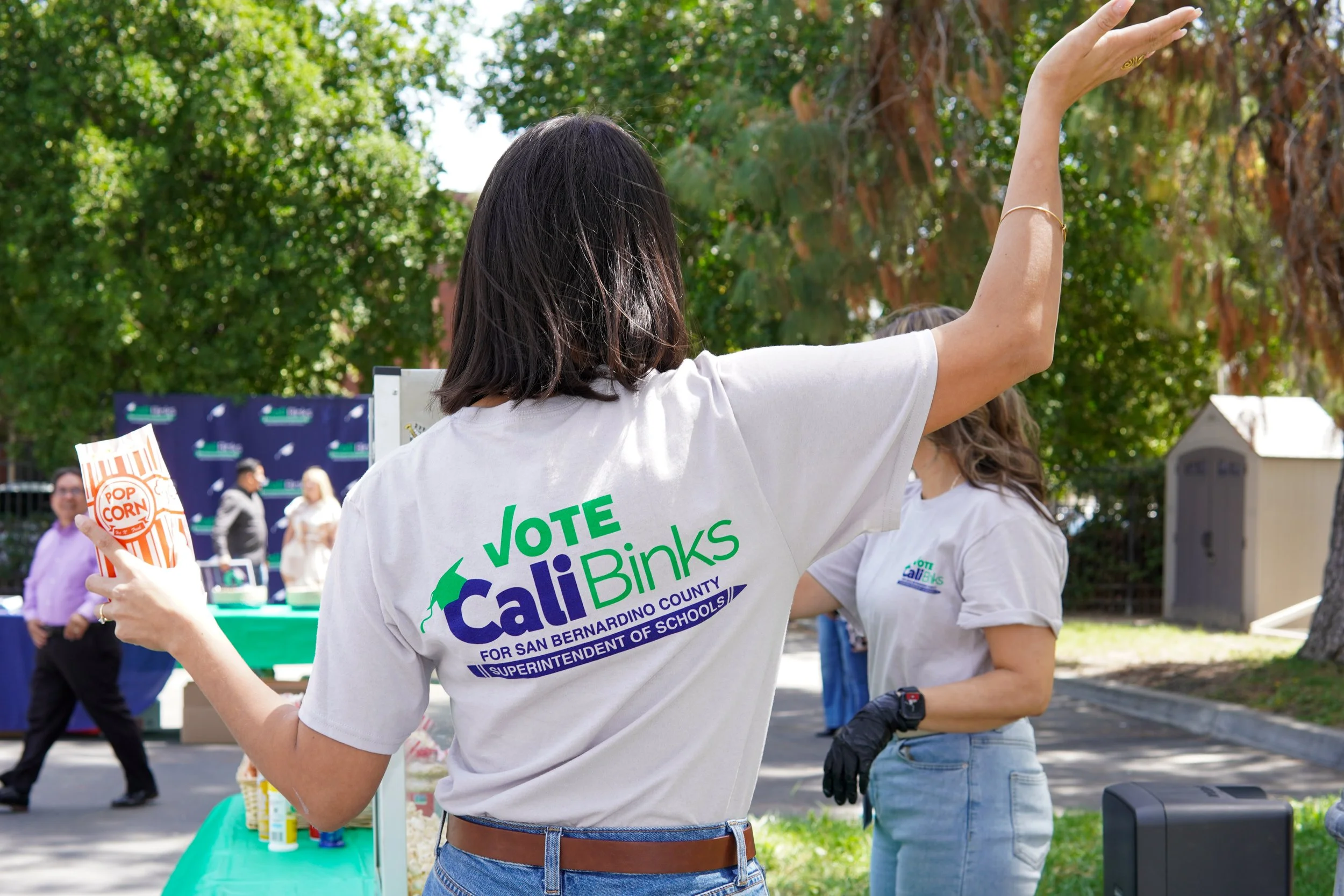 Adult holding a bag of popcorn while wearing a Cali Binks campaign t-shirt.