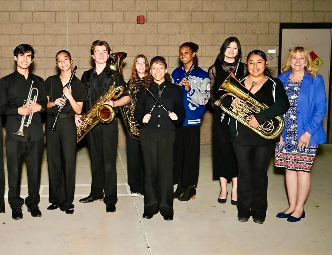 Eight high school students holding instruments and smiling while standing next to Cali.