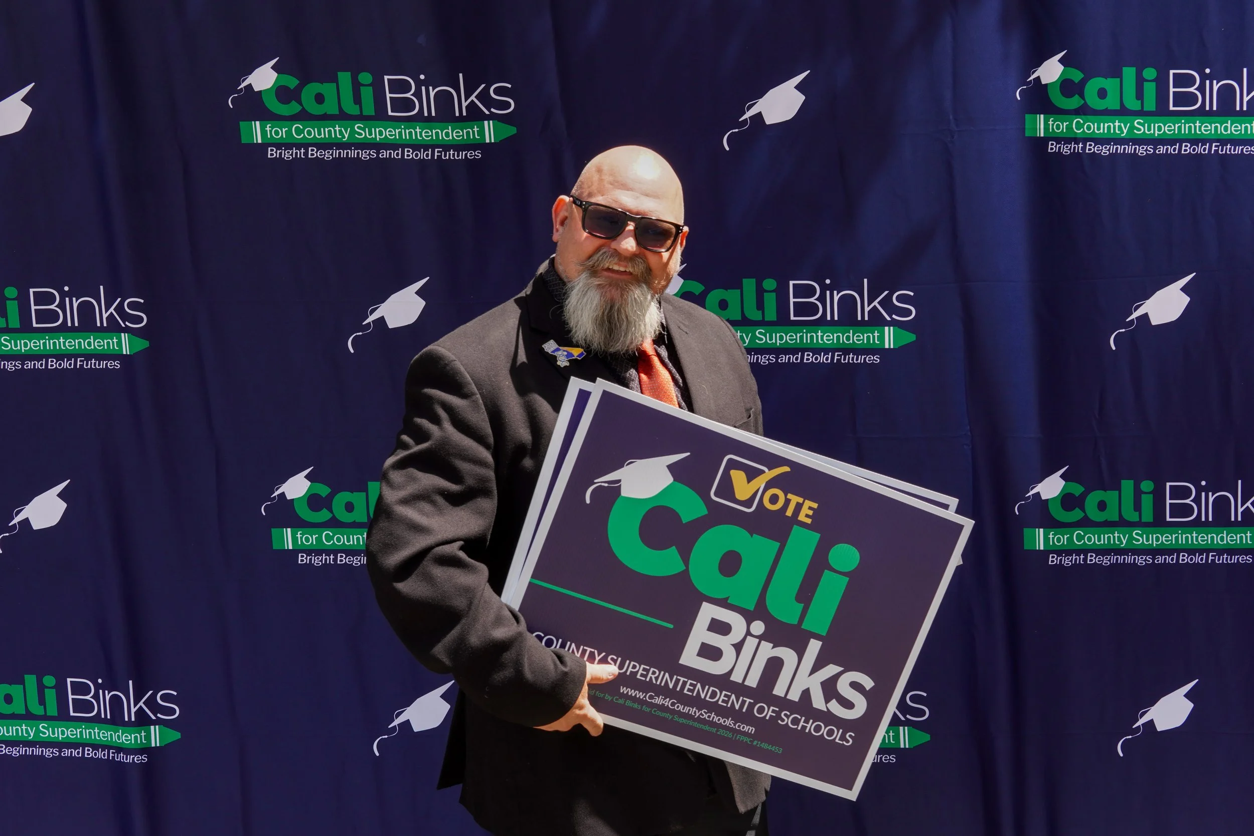 Adult holding a few yard signs in front of the step and repeat with the campaign logo.