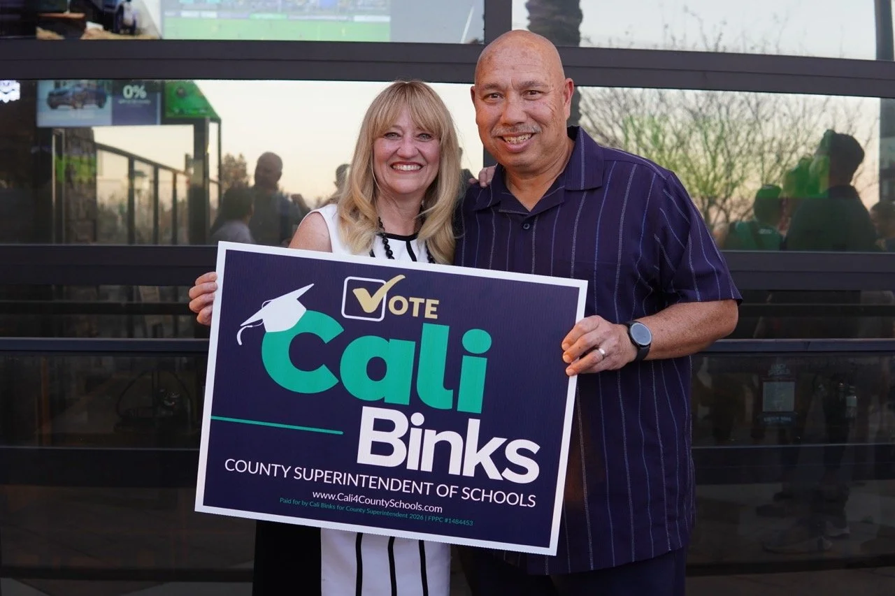 Cali posing with Mars Serna, holding a yard sign.
