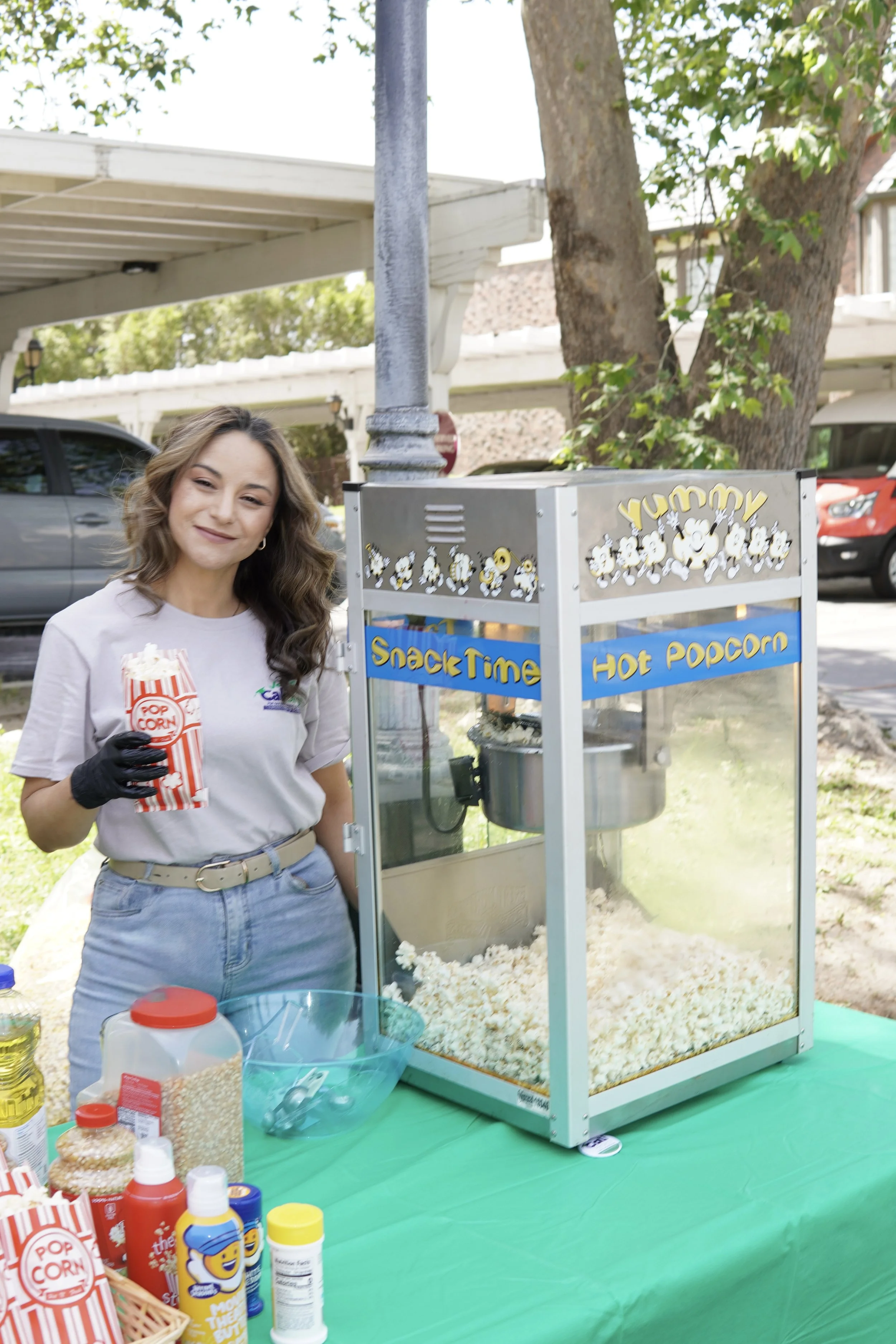 Adult standing next to a popcorn machine while holding a bag filled with popcorn.