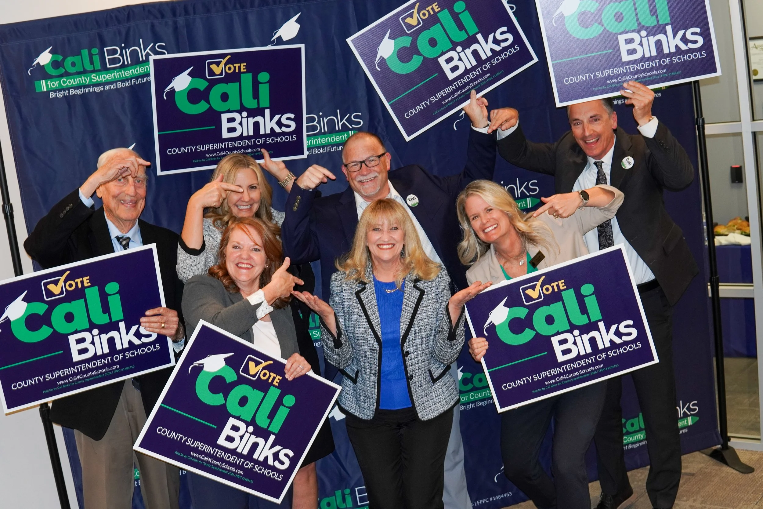 Group of people holding yard signs and pointing to Cali Binks in the center.