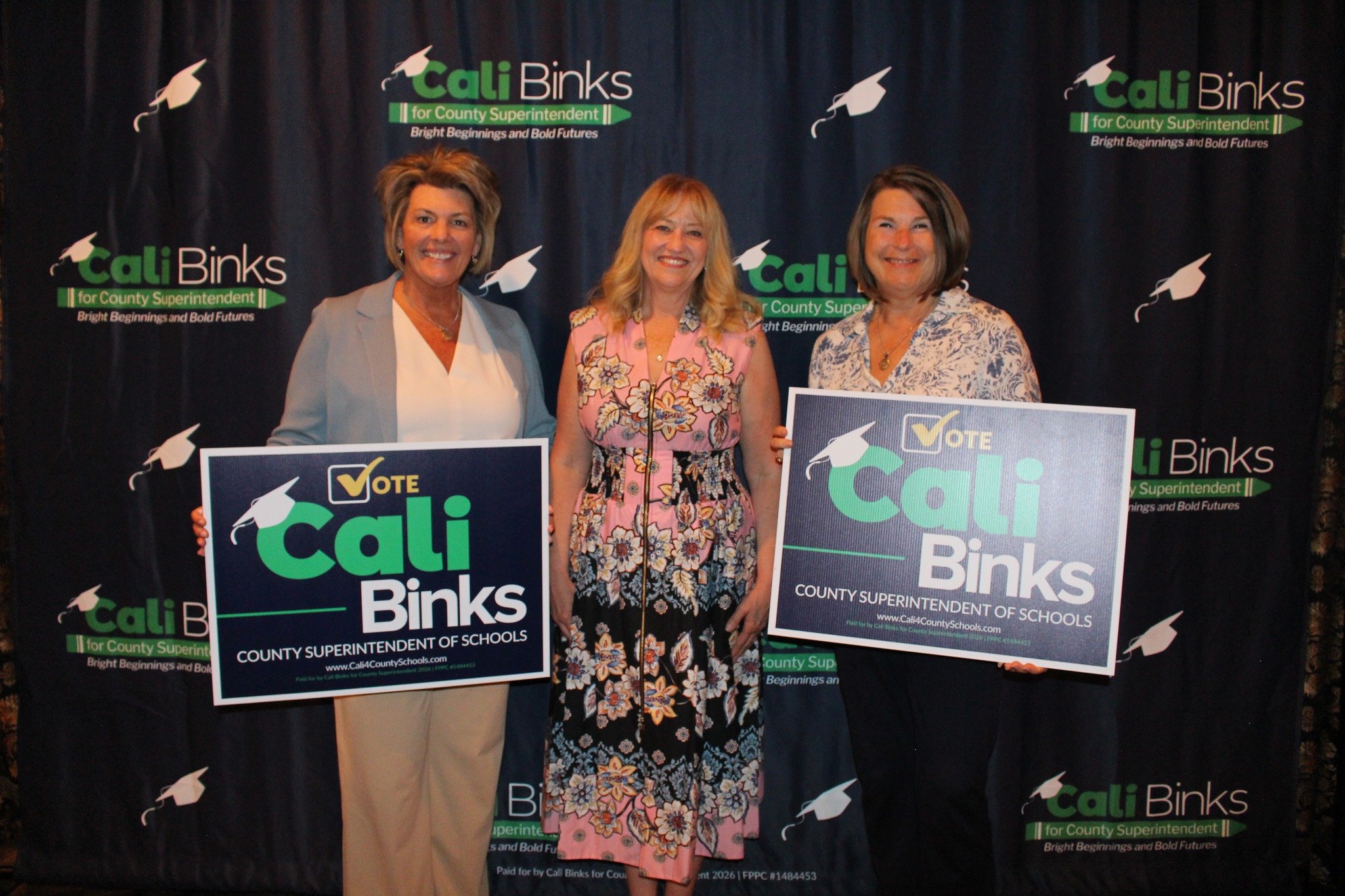 Cali Binks with two guests holding a yard sign promoting her campaign.