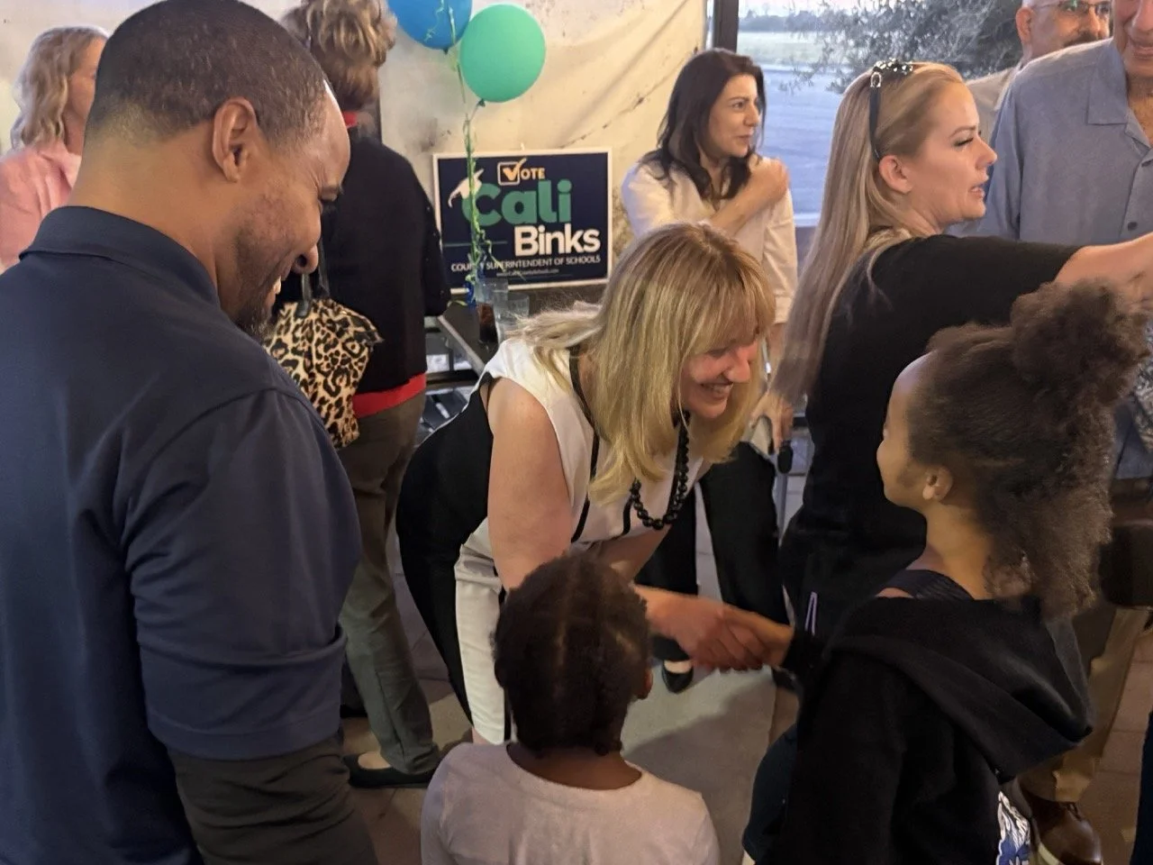 Cali shaking hands with a young child while a sibling and dad stand next to them.