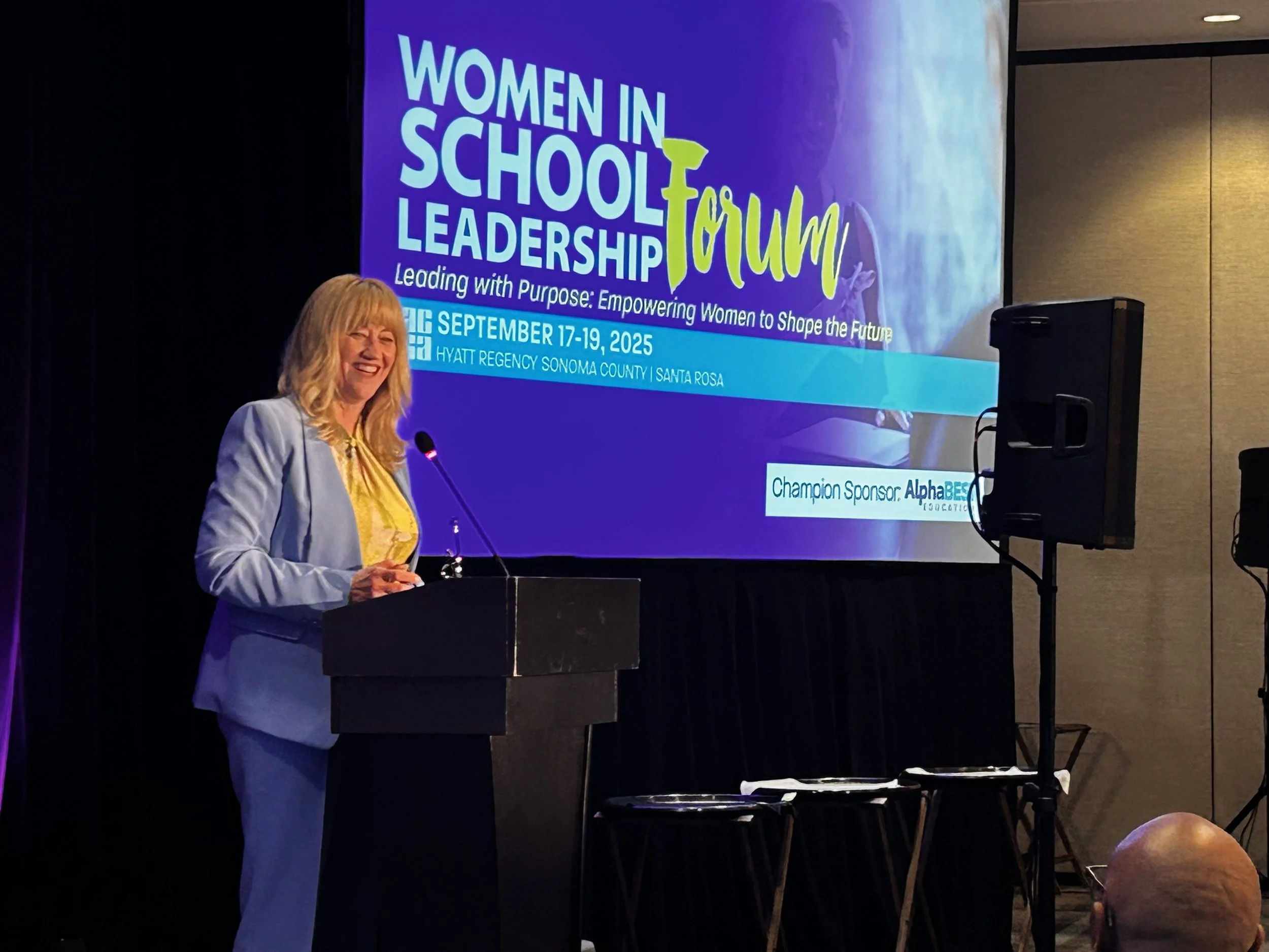Cali behind a microphone and podium receiving the Women in School Leadership award.
