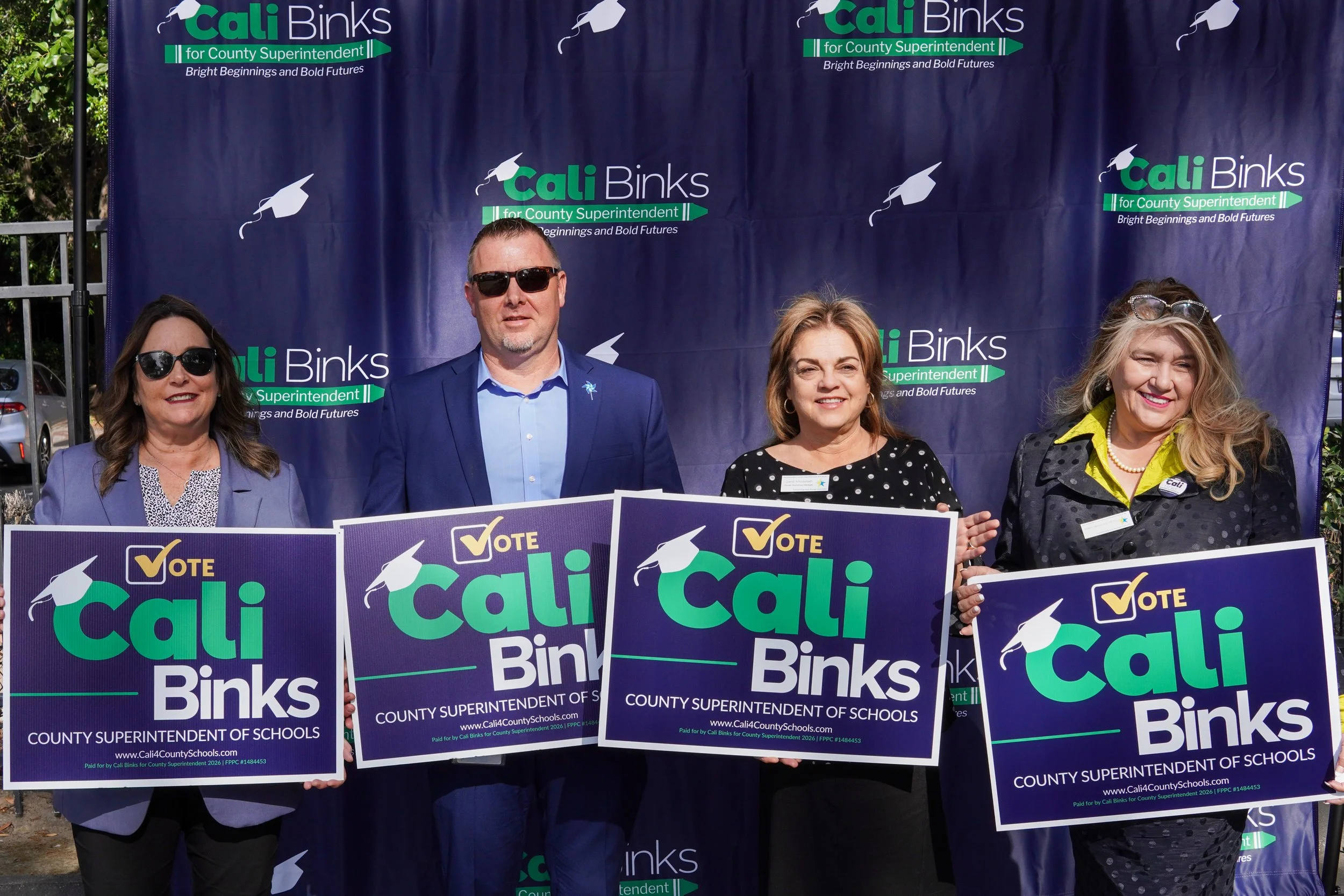 Four adults holding yard signs.